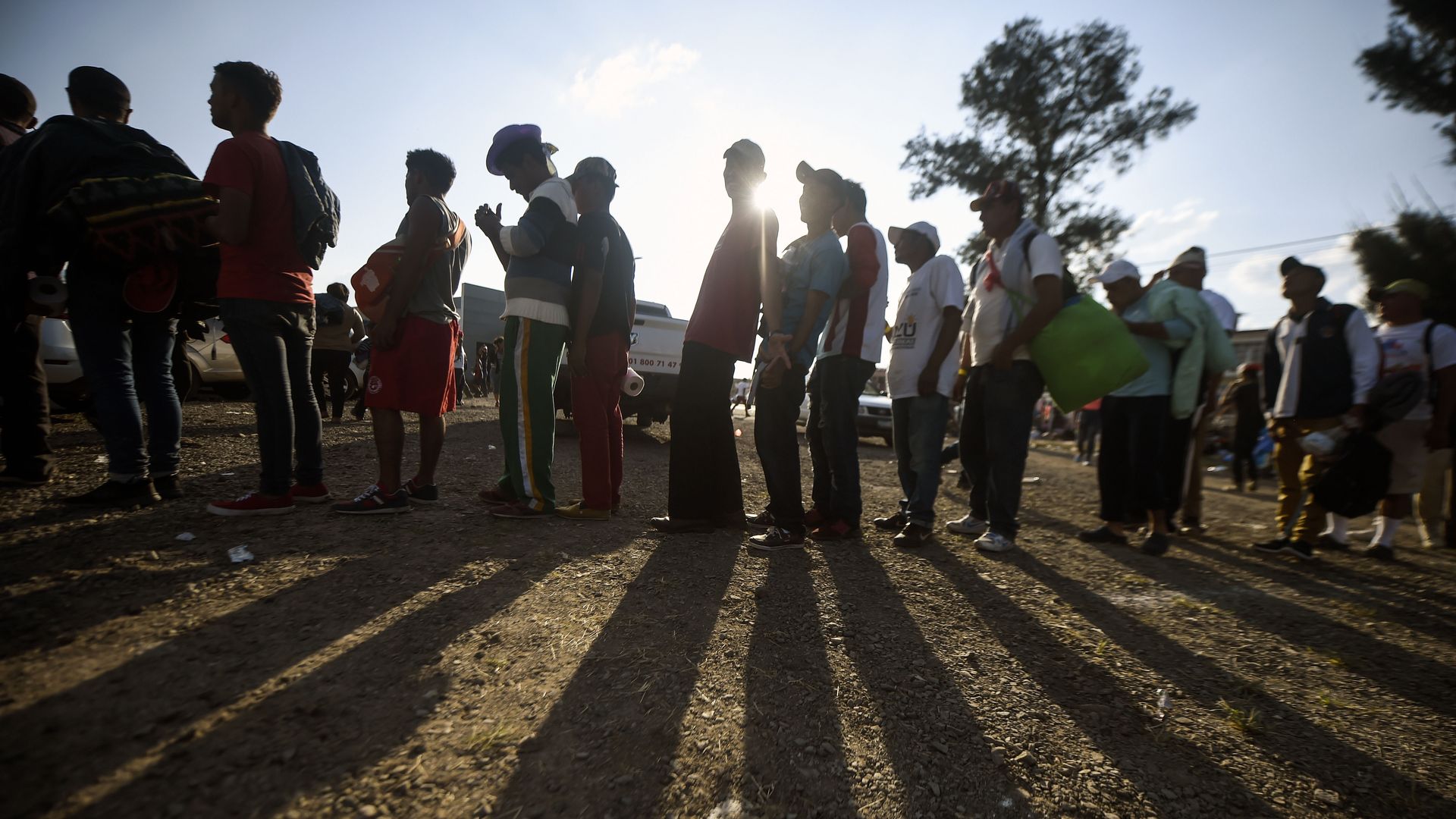 A line of people stand with the sun behind them.
