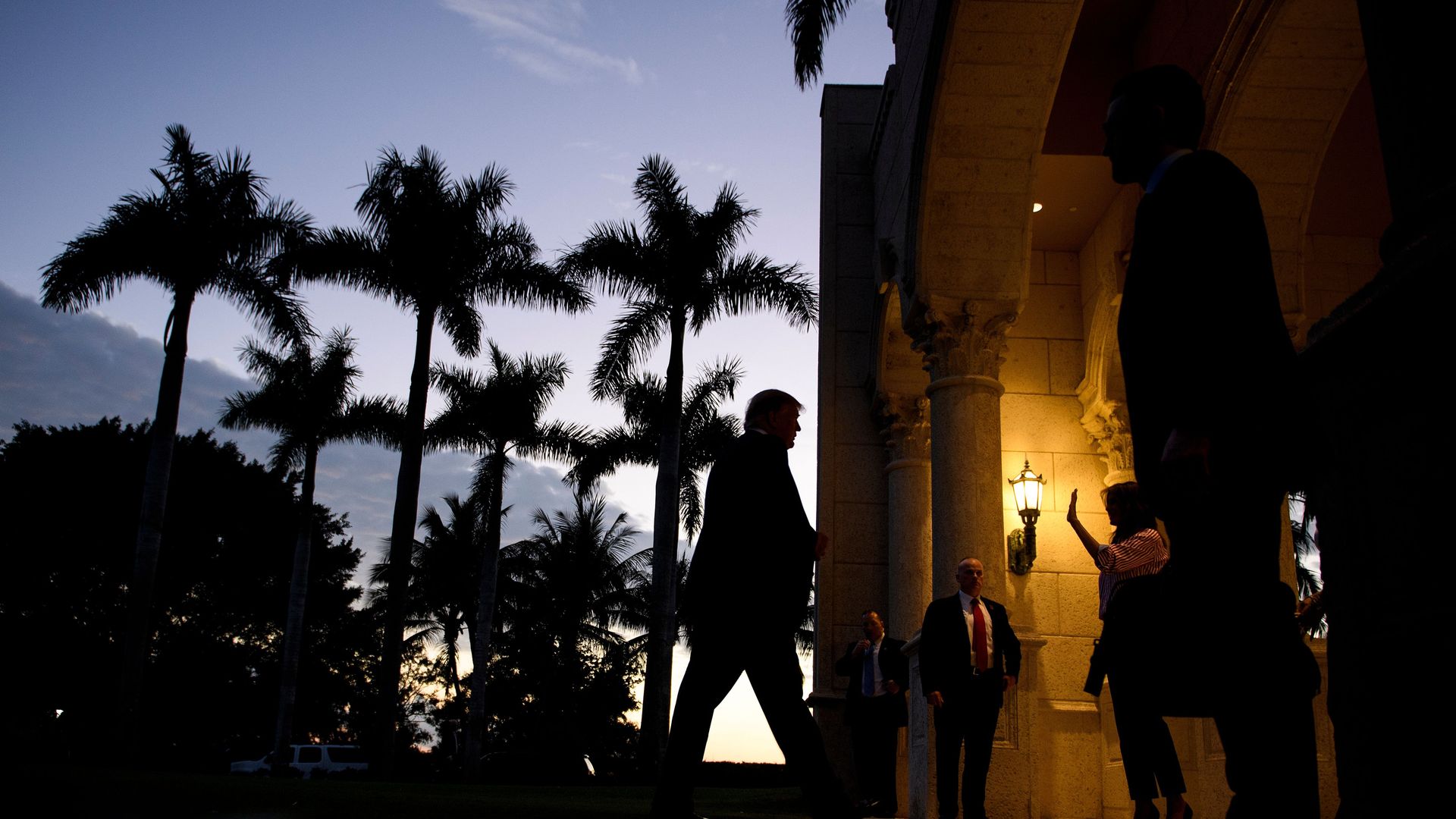 This photo shows Donald Trump walking in Florida, with palm trees in the background as the light fades.