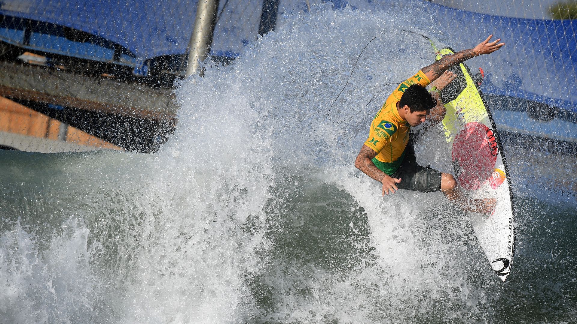 Photo of a surfer carving a wave at a surf park with wired fencing seen in the background