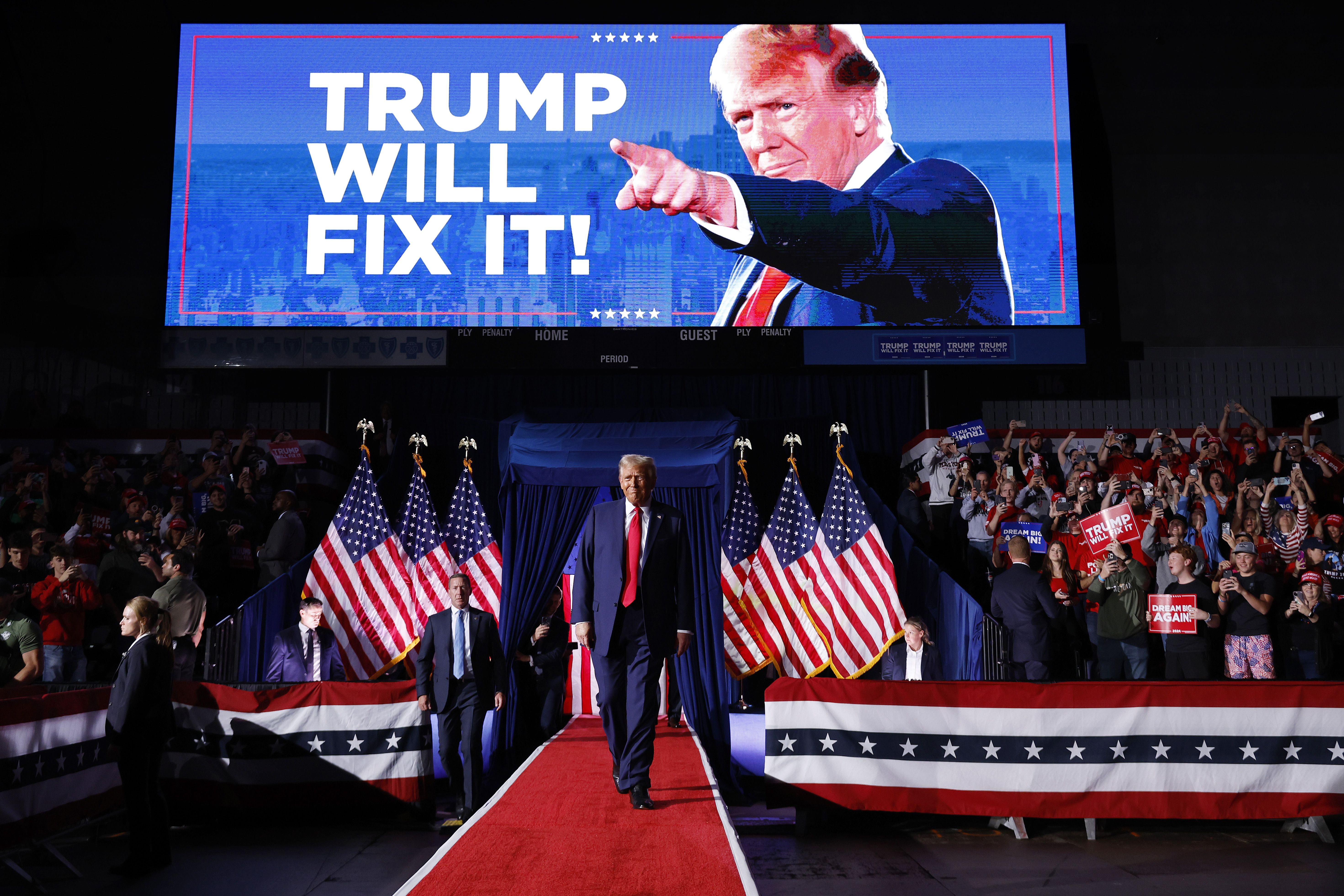 Trump walks in under "TRUMP WILL FIX IT!" sign