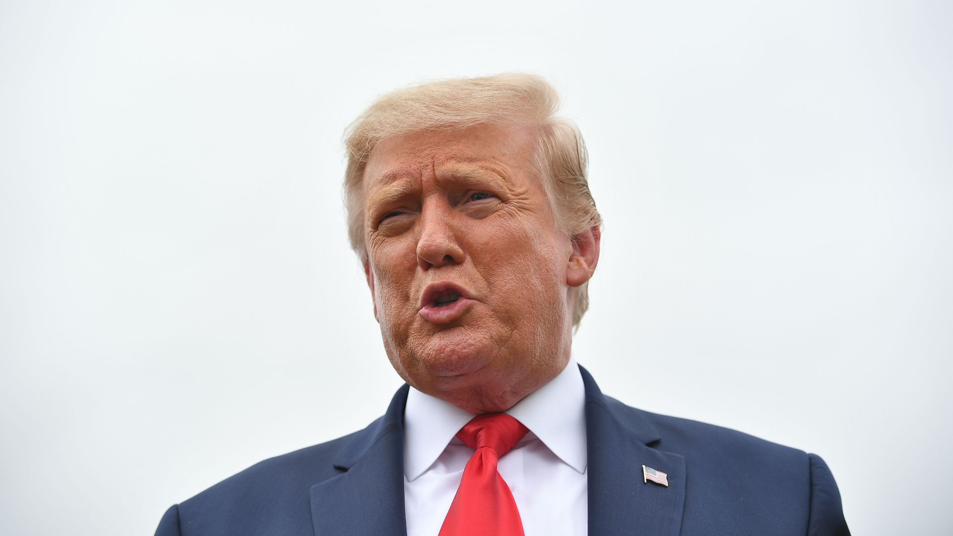 Trump stands in a suit and tie while speaking