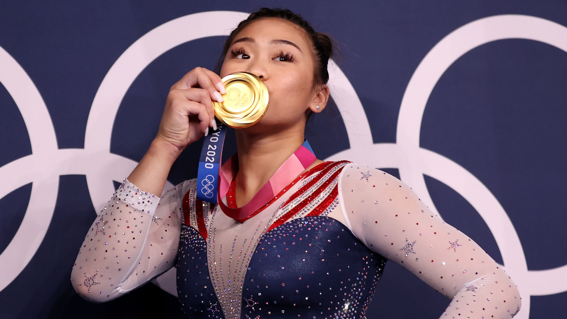 Suni Lee kisses her hold medal in front of the Olympic rings