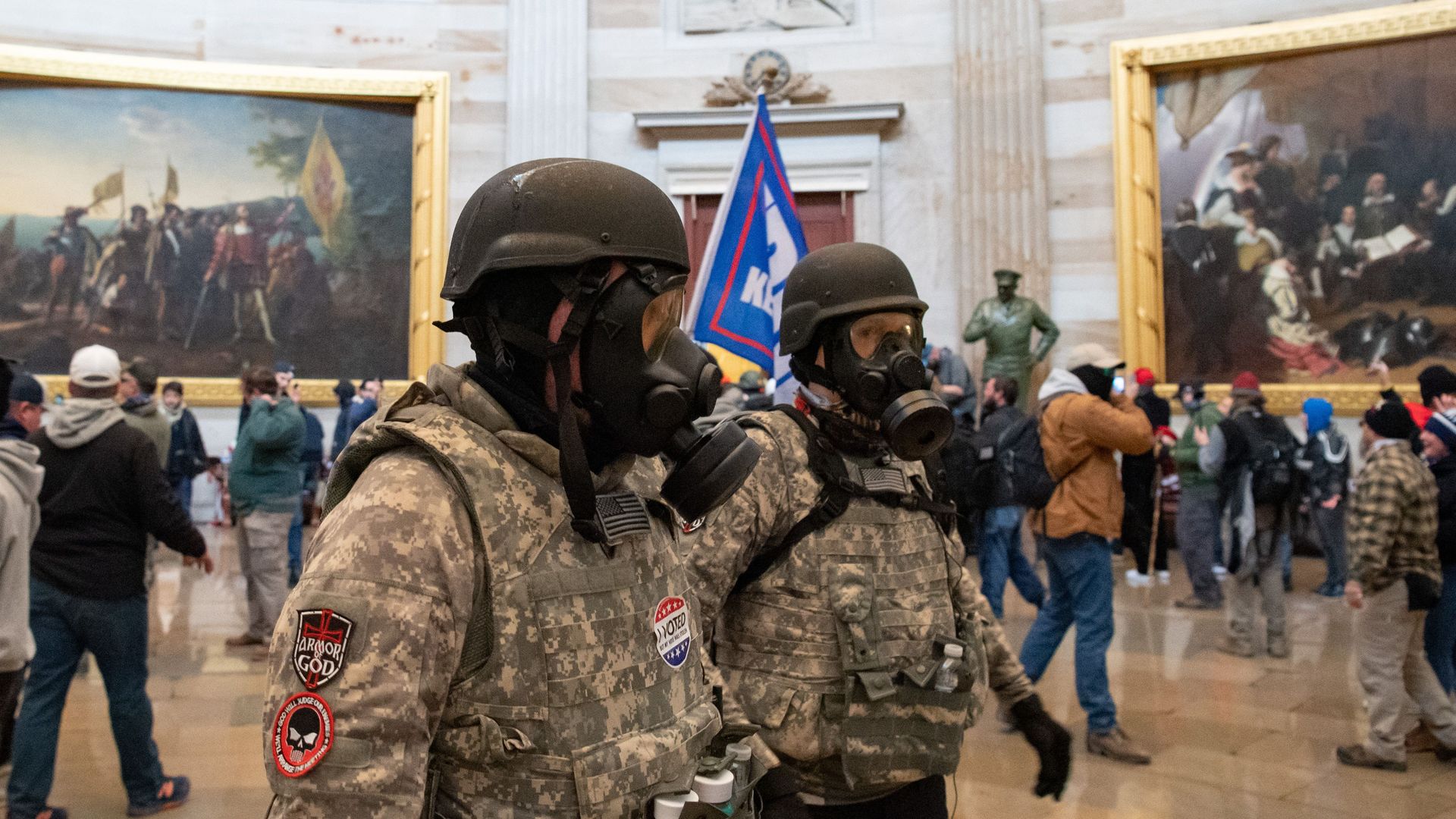 Two people wearing gas masks, helmets and fatigues walk through the Capitol 