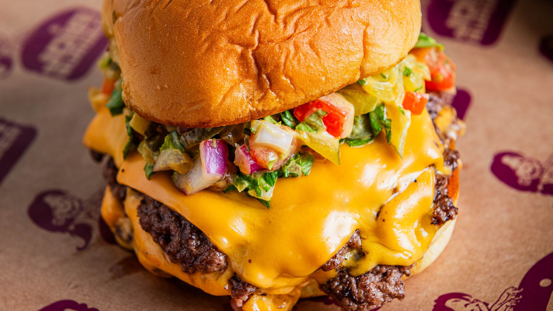 A double-patty smashburger with melted cheese and a chop of lettuce, onion and tomato on top