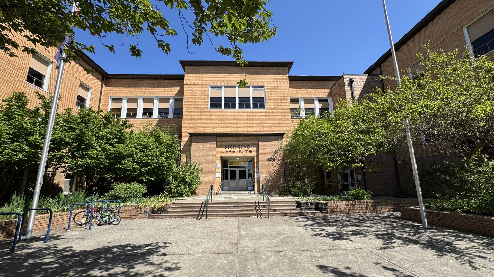 Image shows the front of a brick school building with trees lining the front.