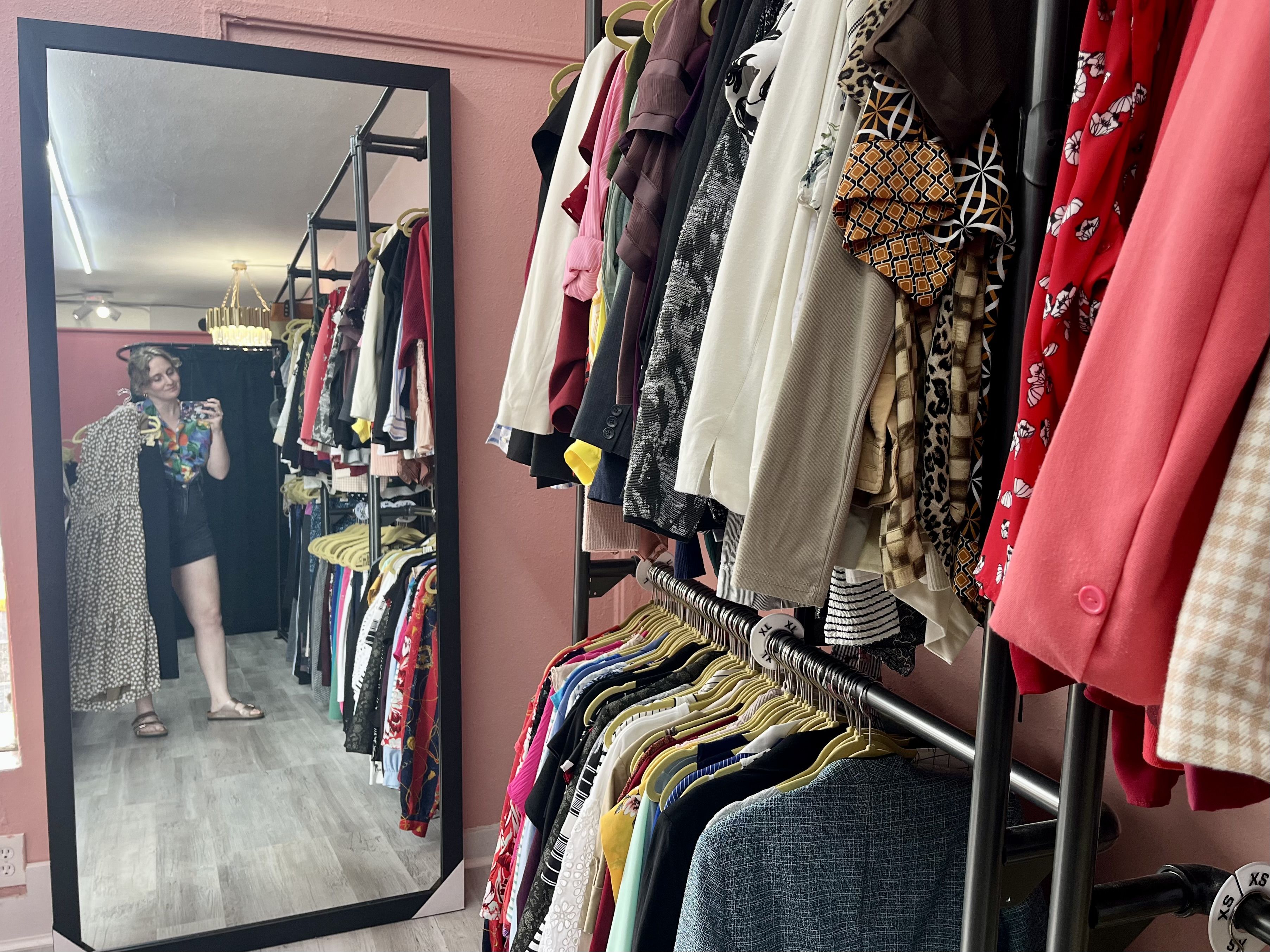 A woman taking a mirror selfie next to racks of clothing.