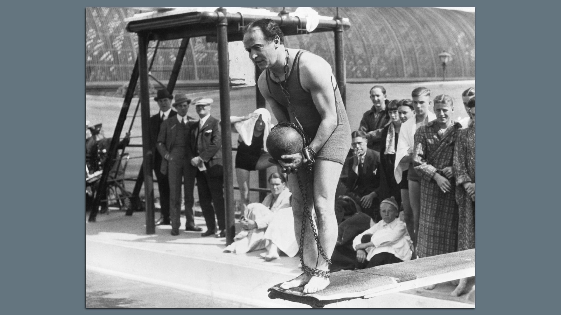 Houdini on a diving board chained up with a metal ball, with onlookers watching