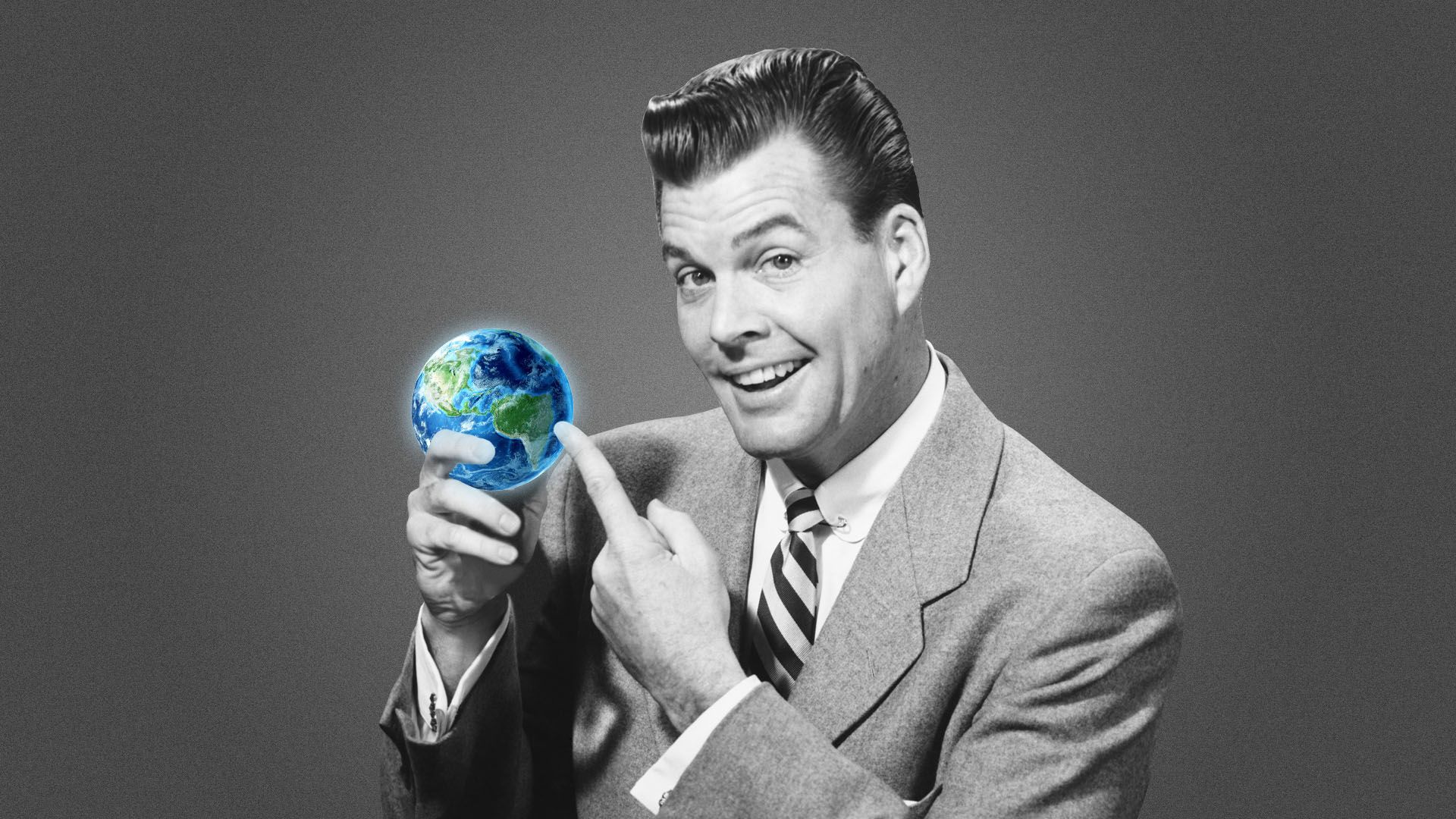 Man who looks like a corporate executive holding a small Earth-shaped ball and pointing to it.