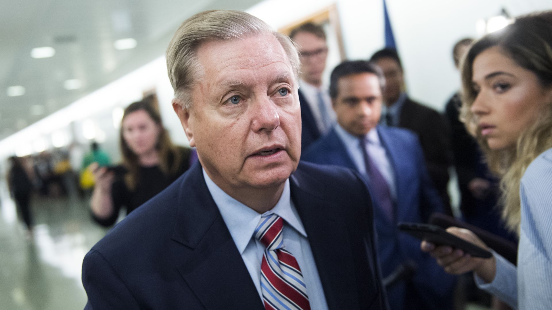 In this image, Graham walks through a hallway crowded with reporters.