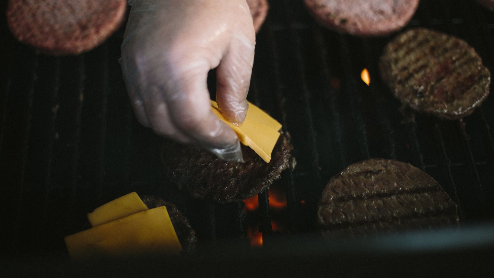 Someone places cheese on burgers on the grill