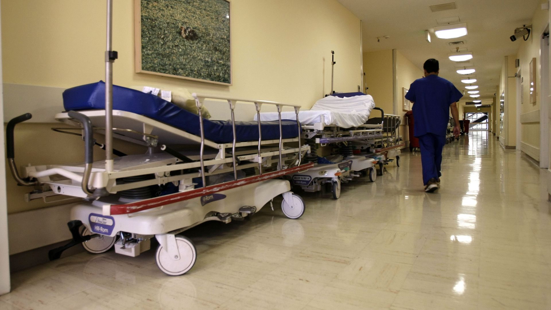 Photo of a health worker walking down a hallway next to hospital beds