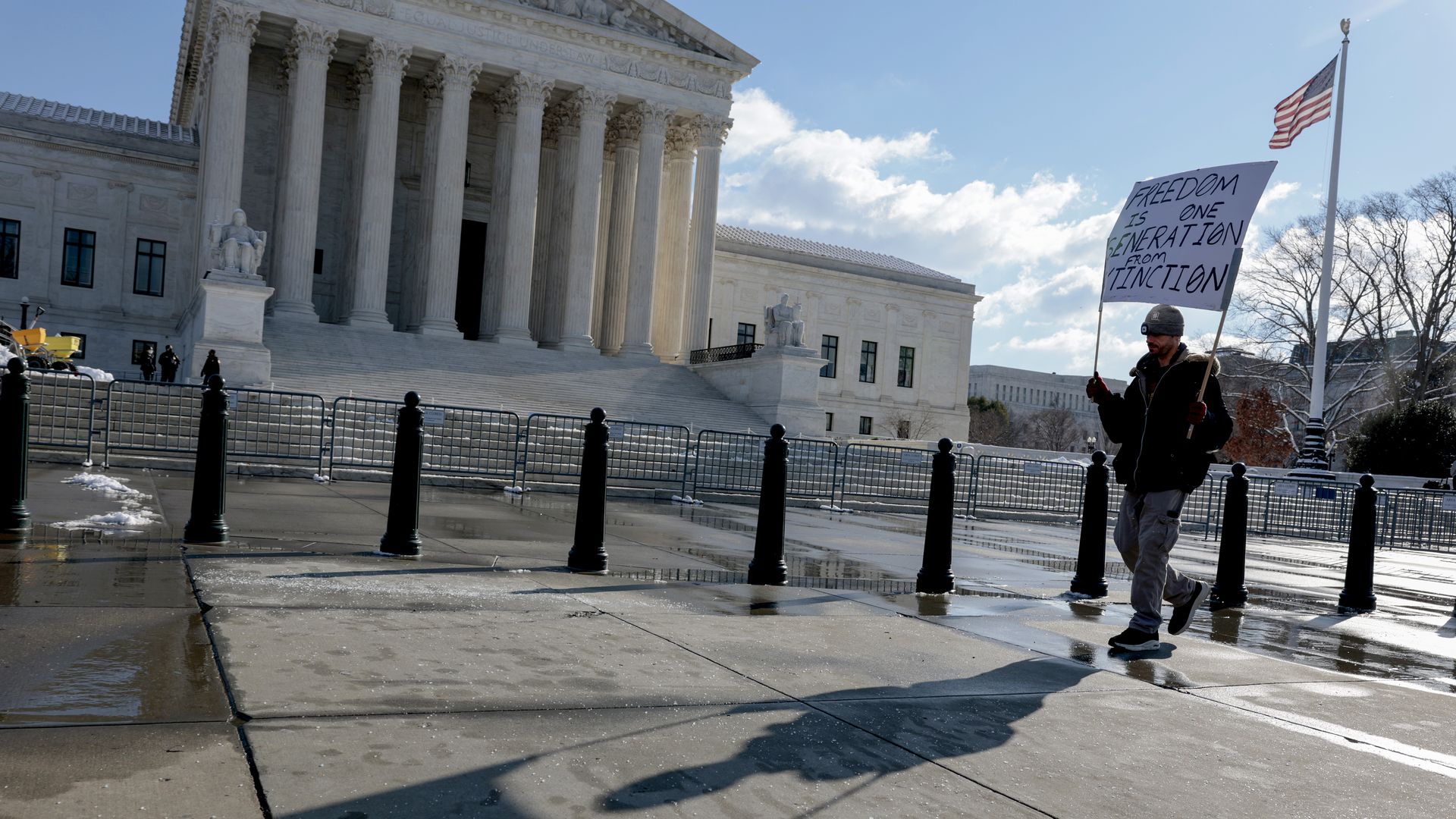 A man holds a sign protesting the president's proposed vaccine mandate on a sunny day outside the Supreme Court.