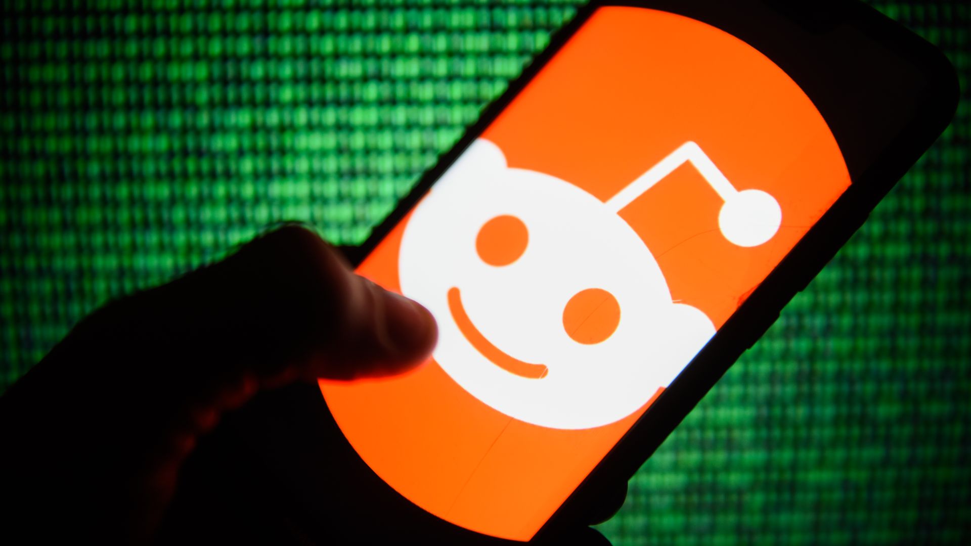 In this image, a person holds a smart phone with the Reddit logo displayed