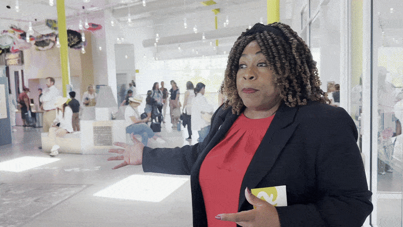 Image shows a woman in a suit gesturing.