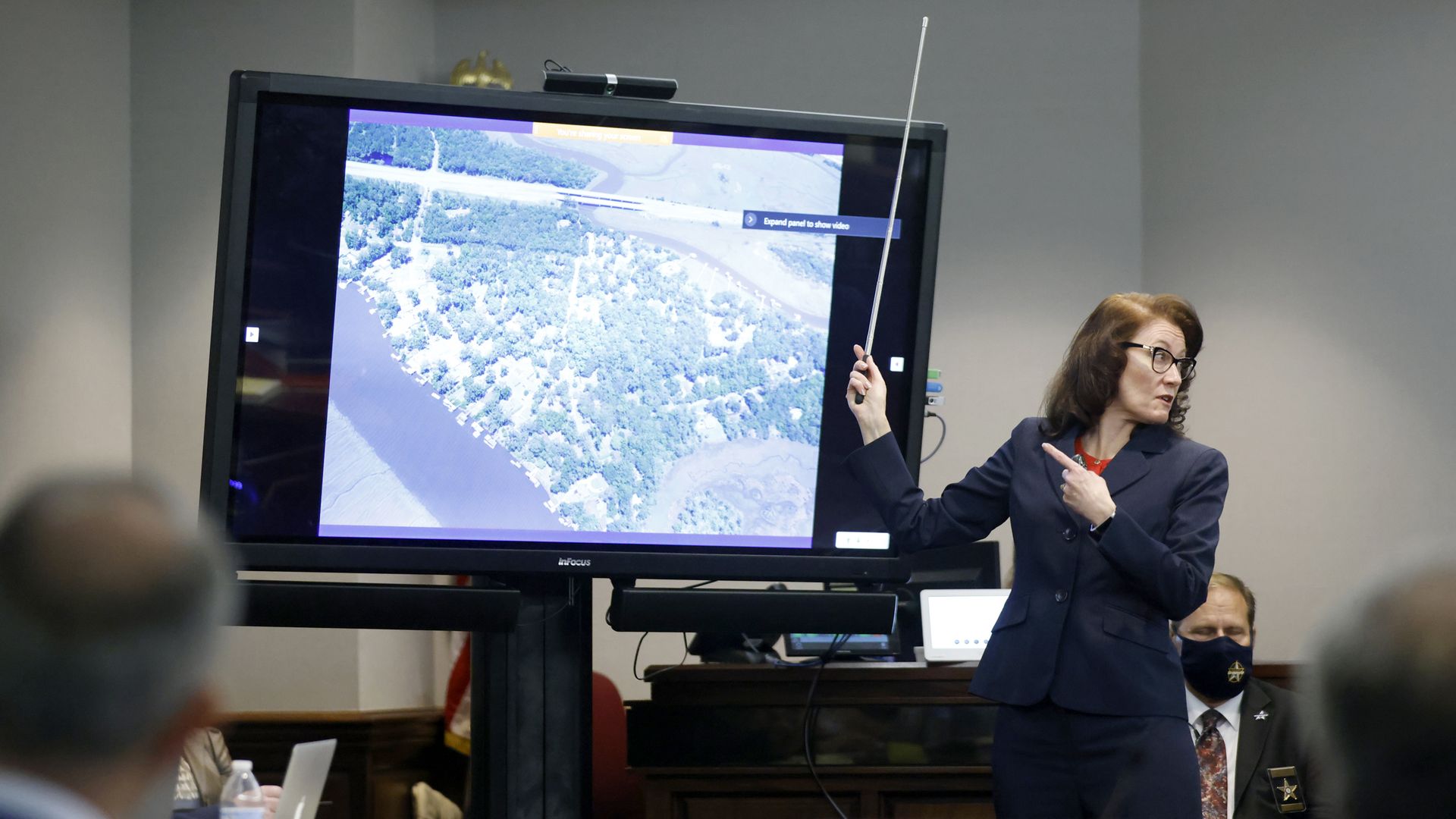 Lawyer with pointer gesturing to map on screen in courtroom