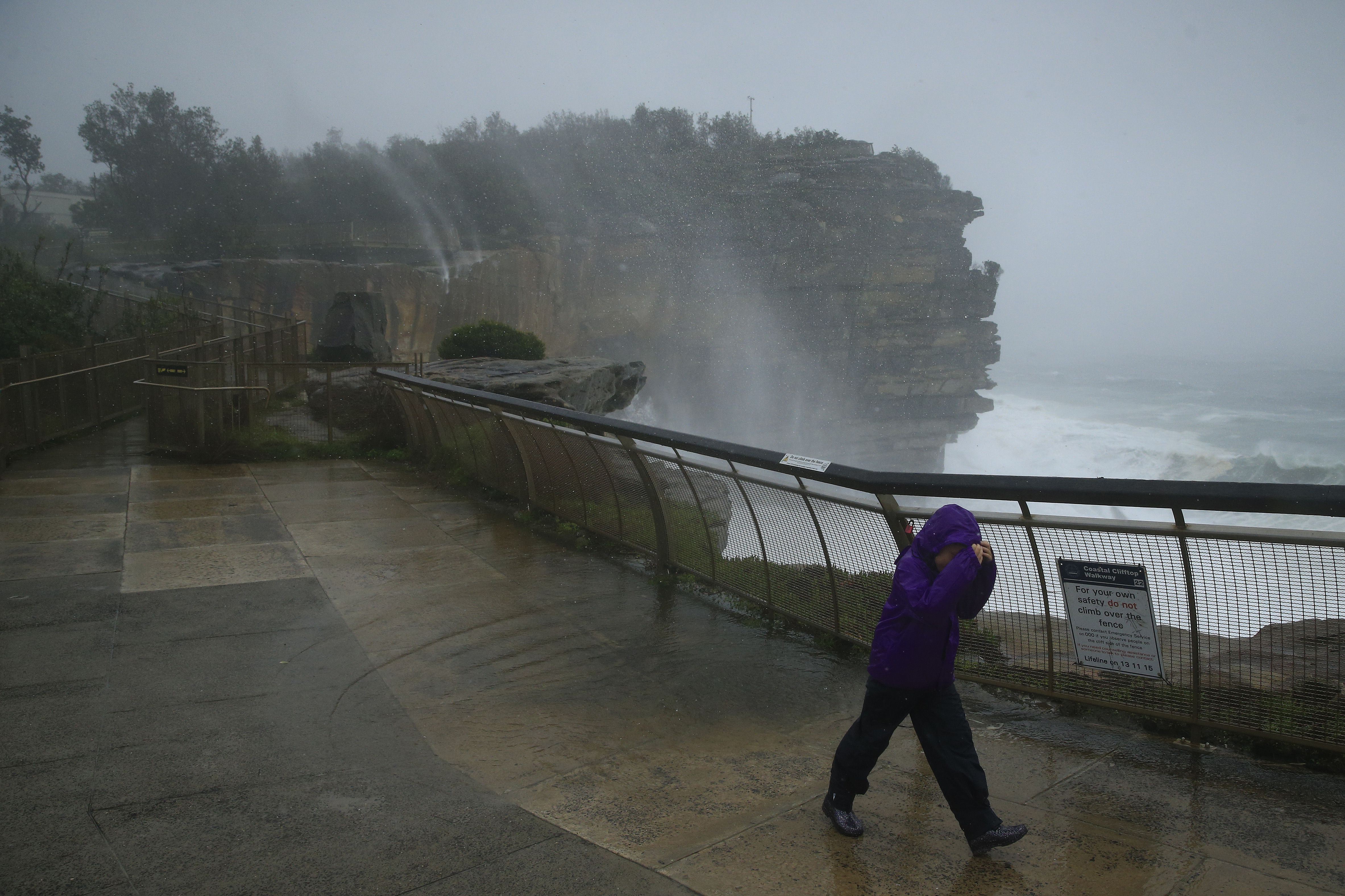 Water rises off the cliffs at Watsons Bay as a sightseer struggles in the wind on February 09, 2020 in Sydney