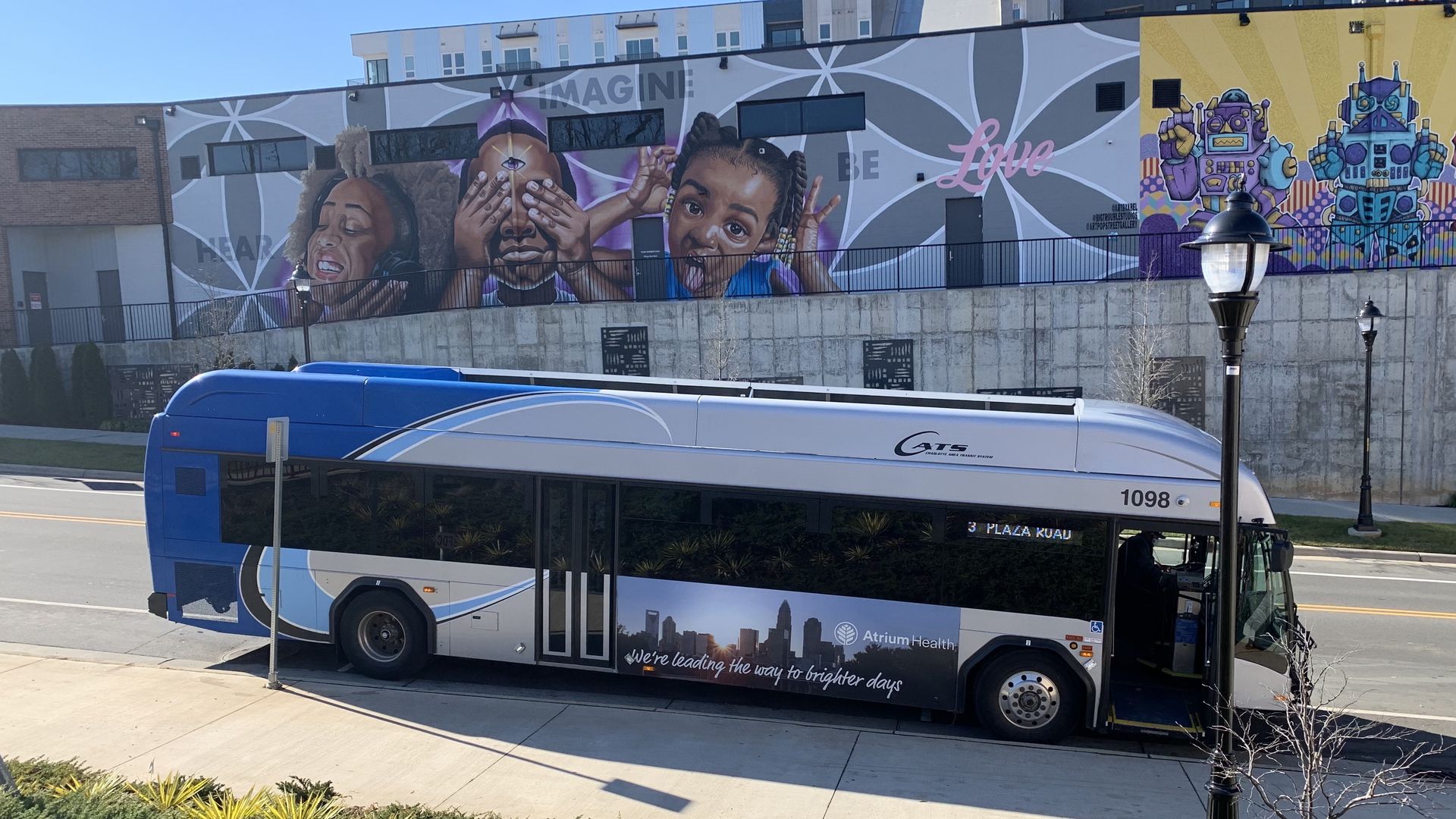 Public bus driving down a hill with a mural of three little girls behind it