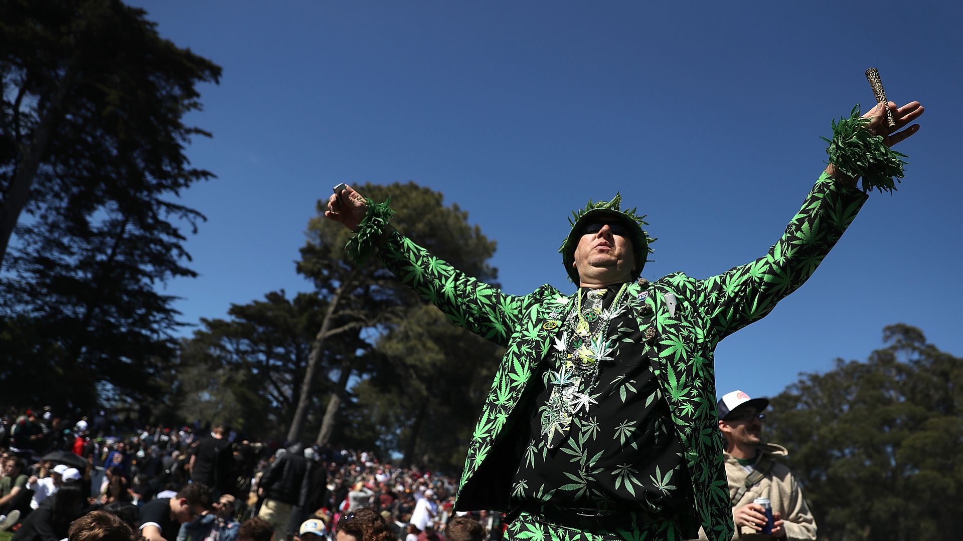 Photo of a person wearing a suit with the pattern of marijuana leaves as they raise their arms while standing in a crowd of partyers