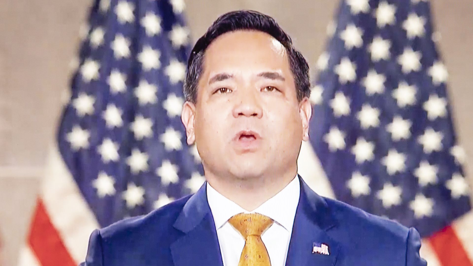 Utah Attorney General Sean Reyes stands in front of two US flags.