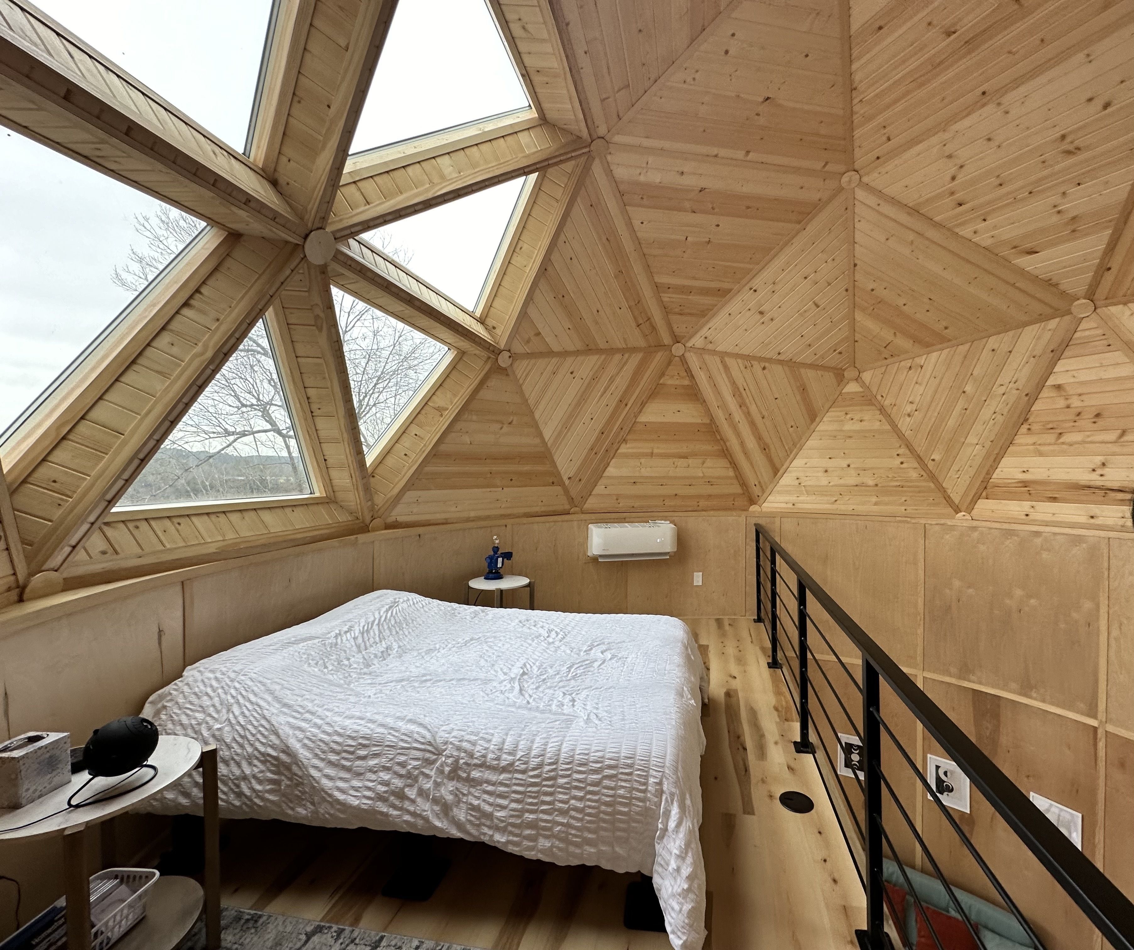 Photo of the bedroom of an Airbnb with the bed under a dome made of wood and windows.