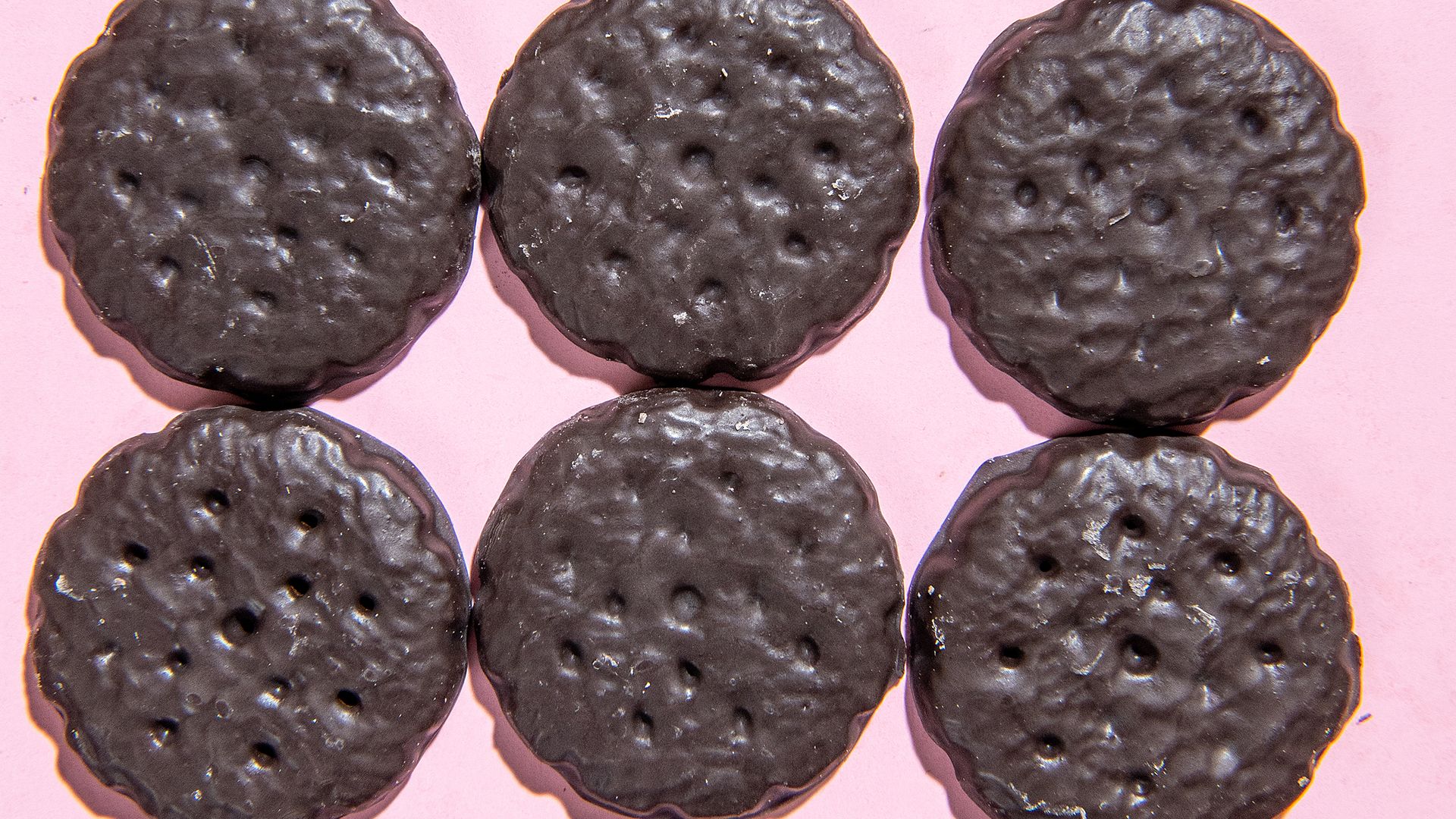 An array of Thin Mints cookies lined up on a pink background. 