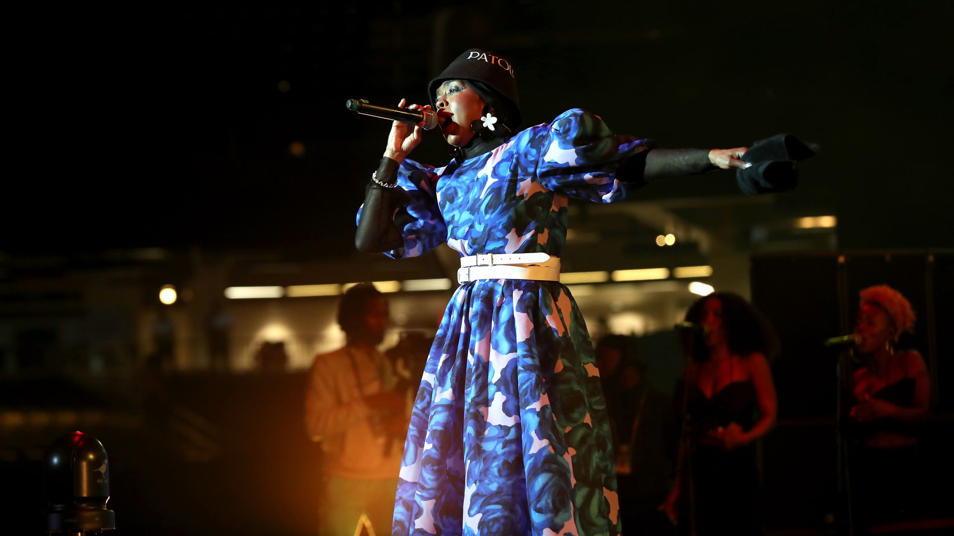 Ms. Lauryn Hill holds a mic to her lips as she performs at Essence Fest 2022, wearing a blue and pink dress with a white belt.