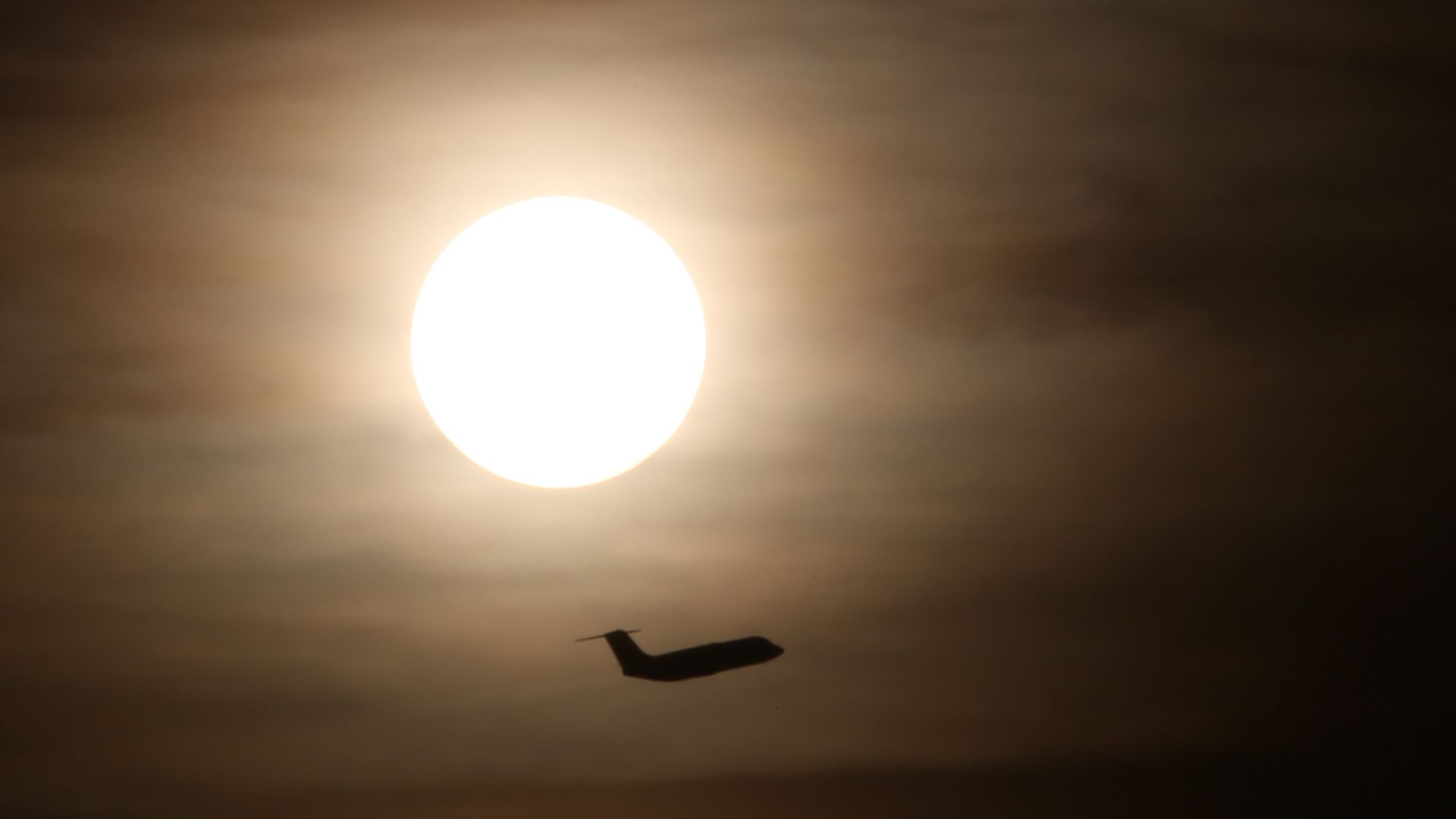 Plane flying across the sky with sun in the distance