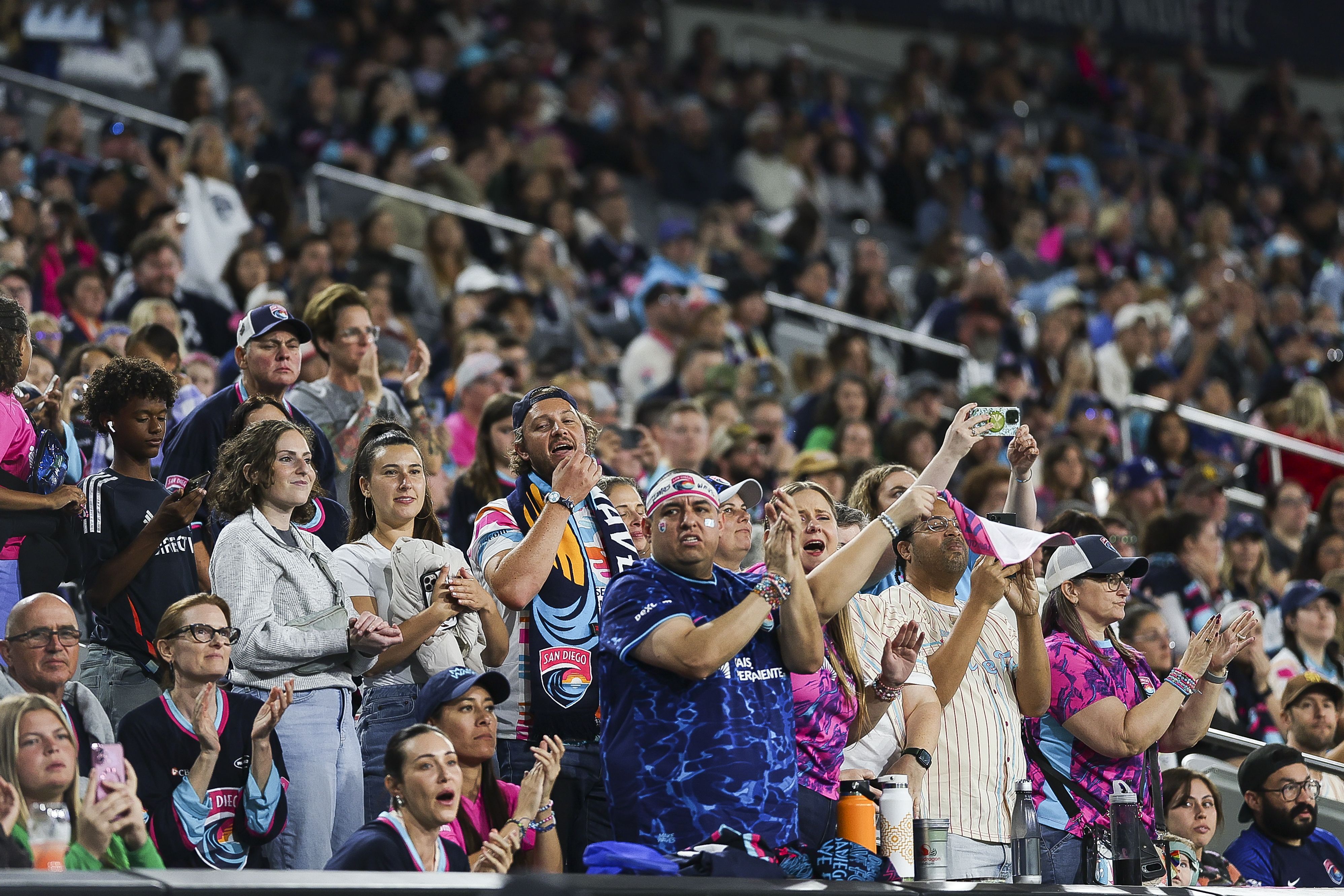 San Diego Wave fans clap and cheer in a crowded section of the soccer stadium. 