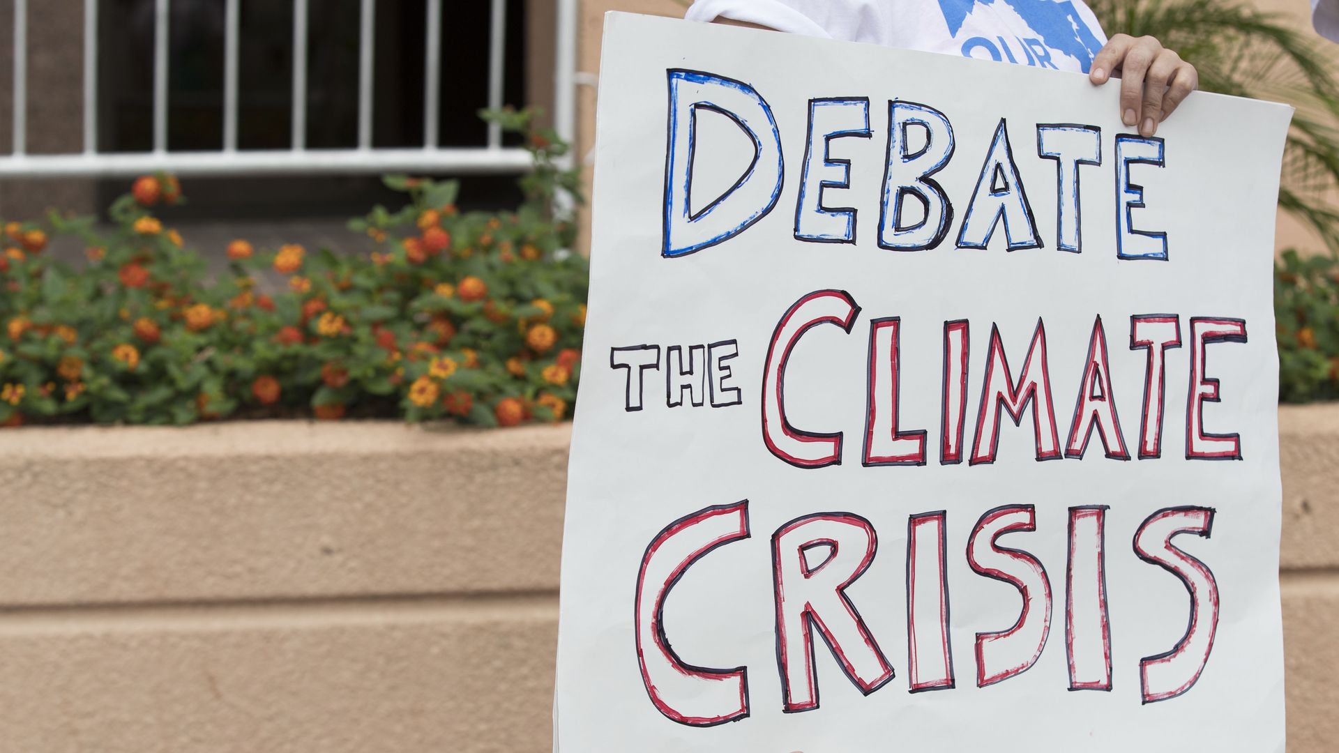 Person holding sign saying "Debate the Climate Crisis"