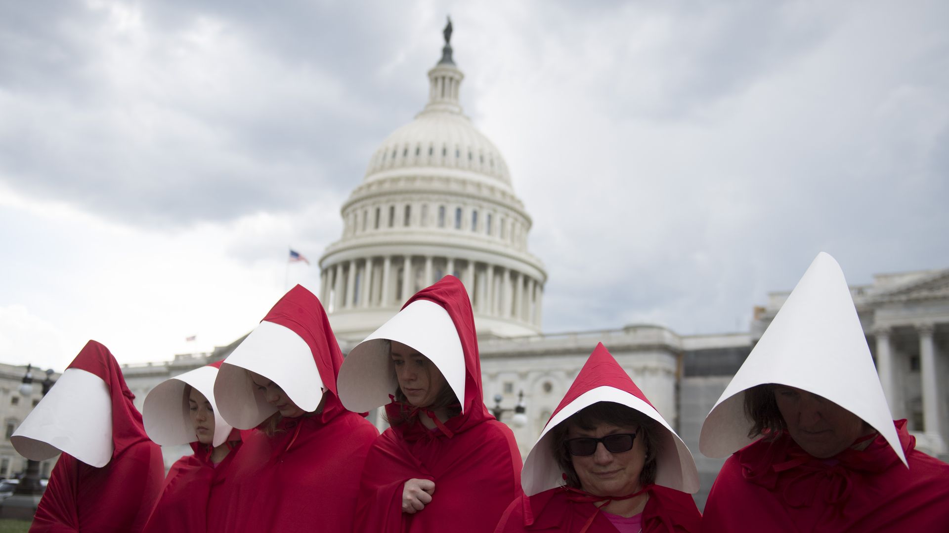 Supporters of Planned Parenthood dressed as characters from The Handmaid's Tale in red clothing and white hats in front of the Capitol Dome.