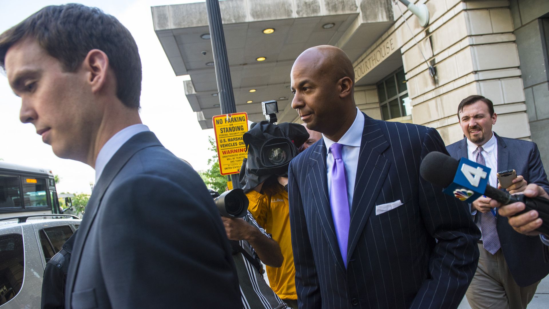 Former D.C. council member Michael A. Brown leaves court, wearing a pinstripe suit and a purple tie, surrounded by television crews and cameras.