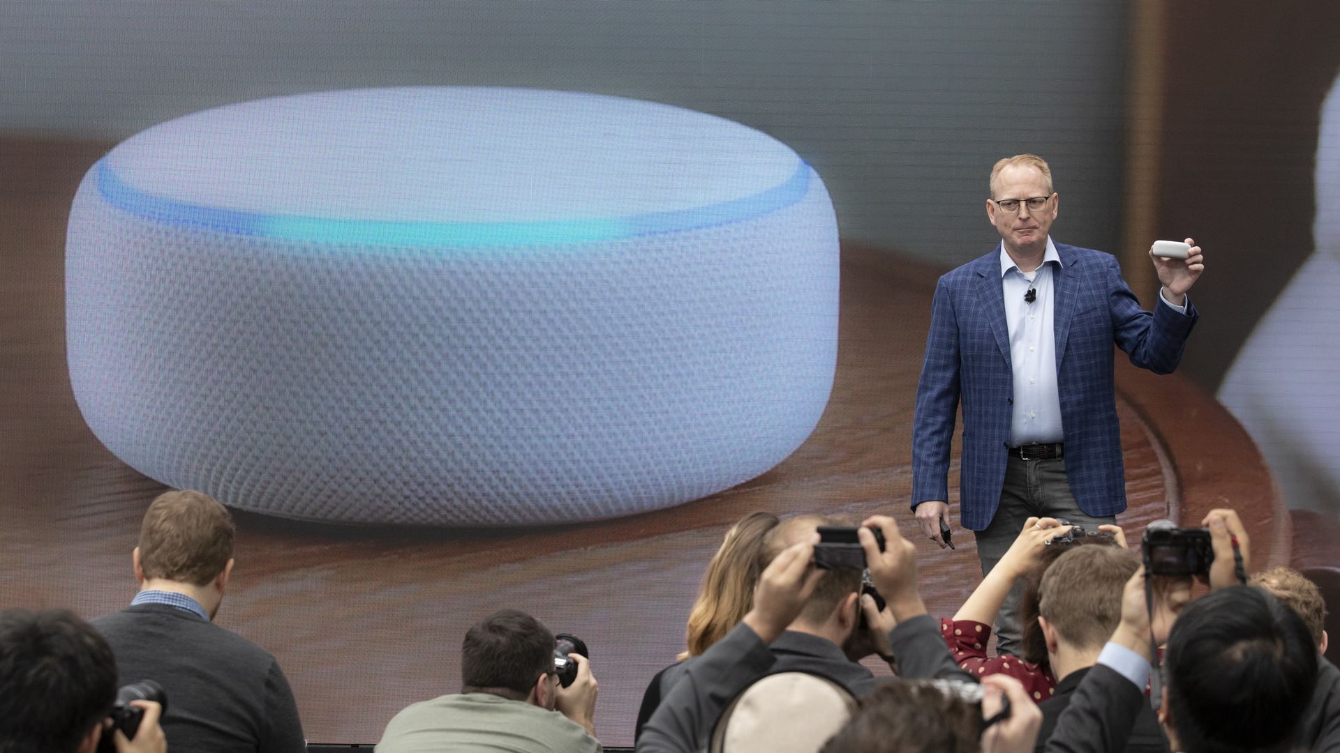 Amazon exec David Limp addressing a crowd while standing next to a giant image of an Alexa smart speaker