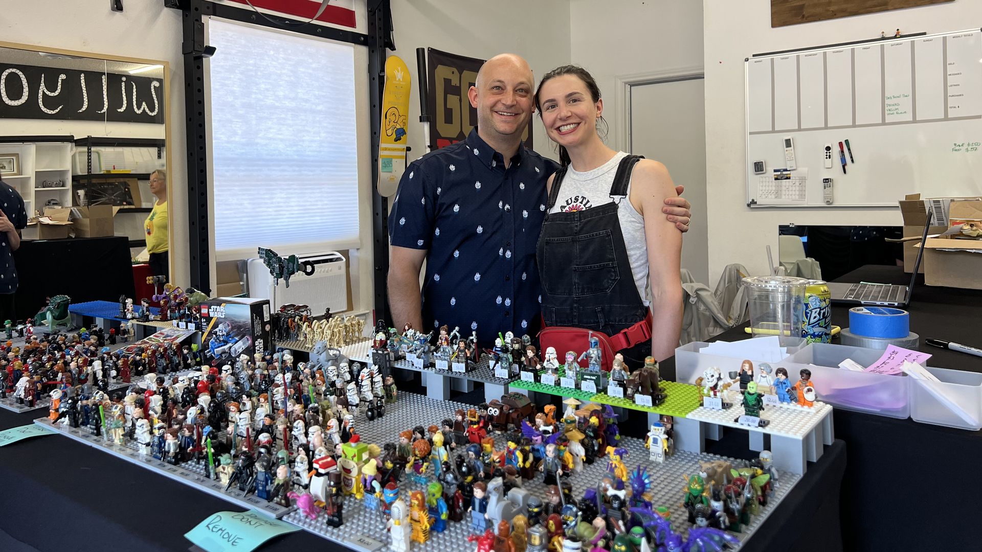 A photo of two people standing in the background with Lego figurines in front of them.