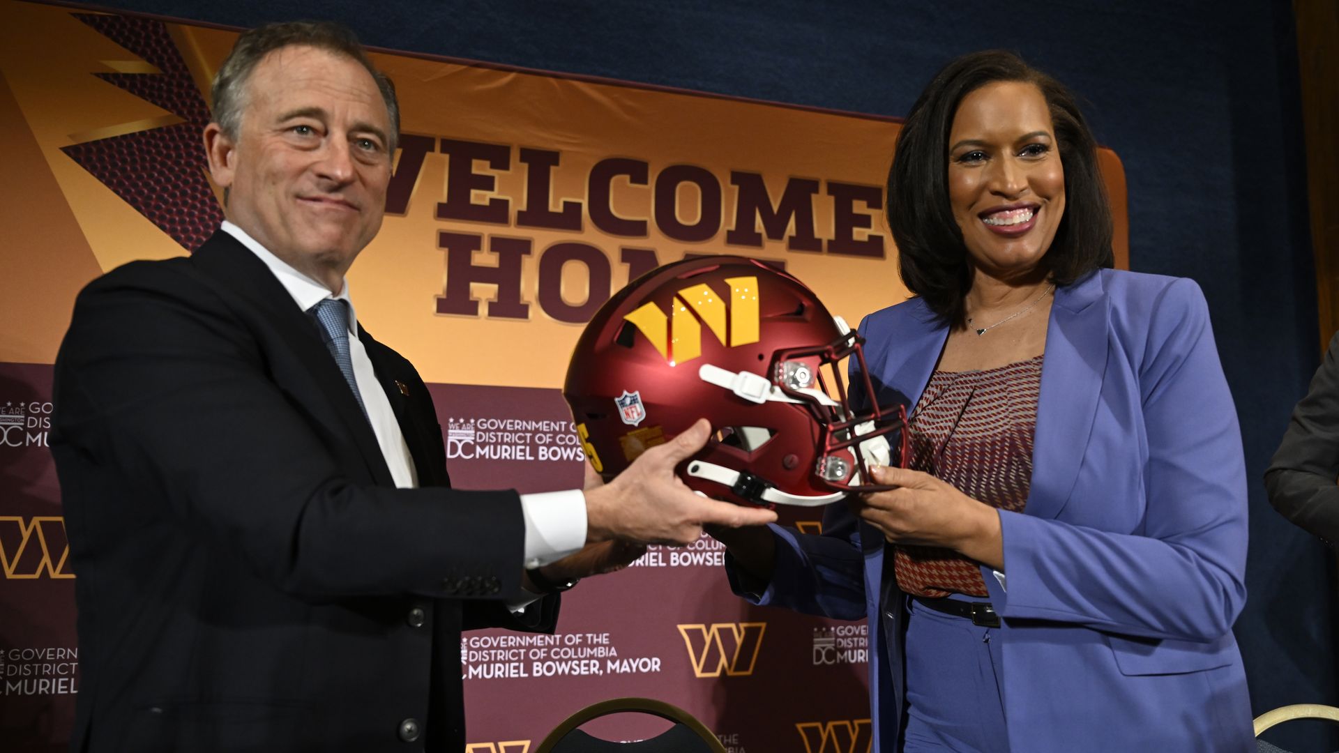 Josh Harris and Mayor Bowser hold a Commanders team helmet