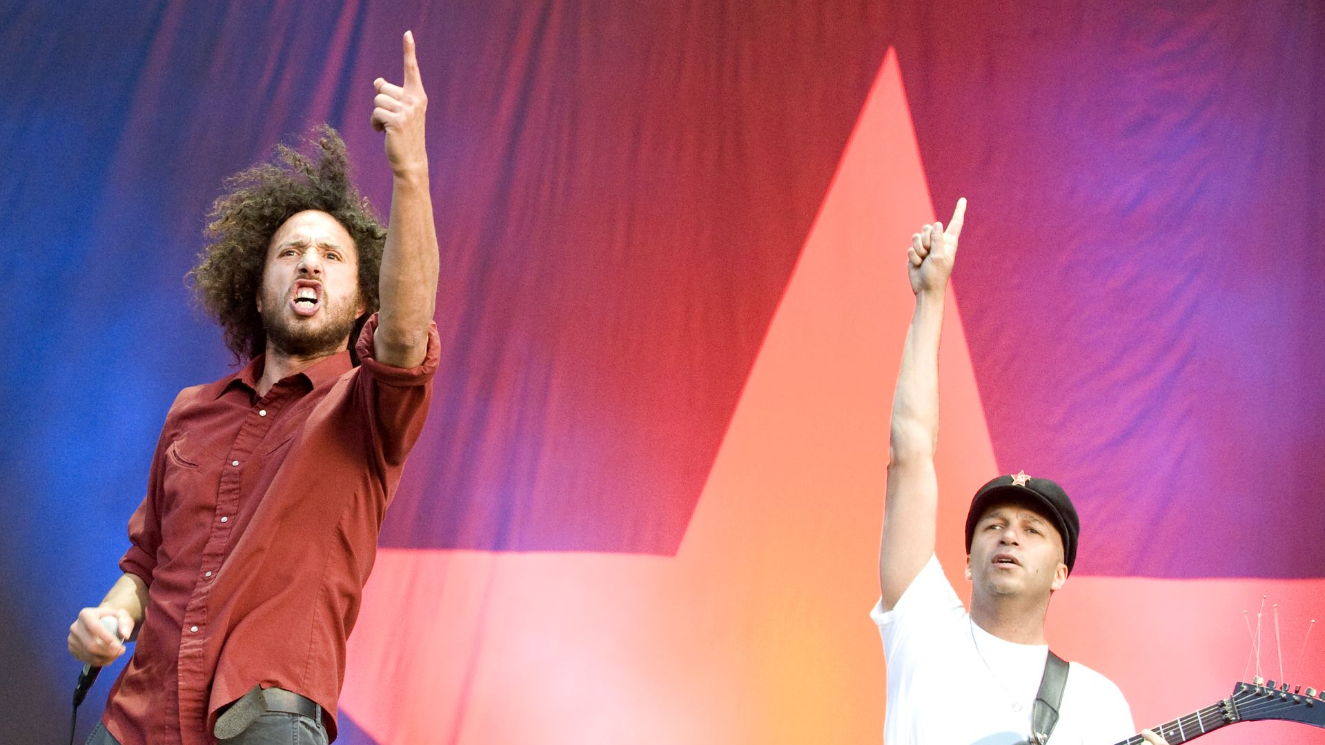 Two members of Rage Against the Machine hold up fingers while on stage. 