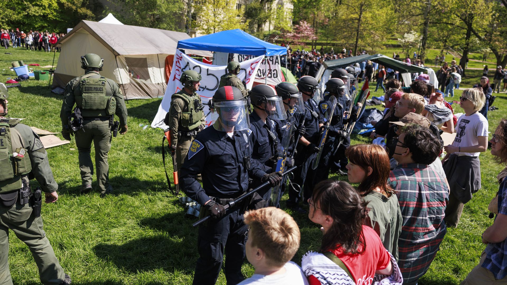 A line of police officers in riot gear face off against a line of demonstrators