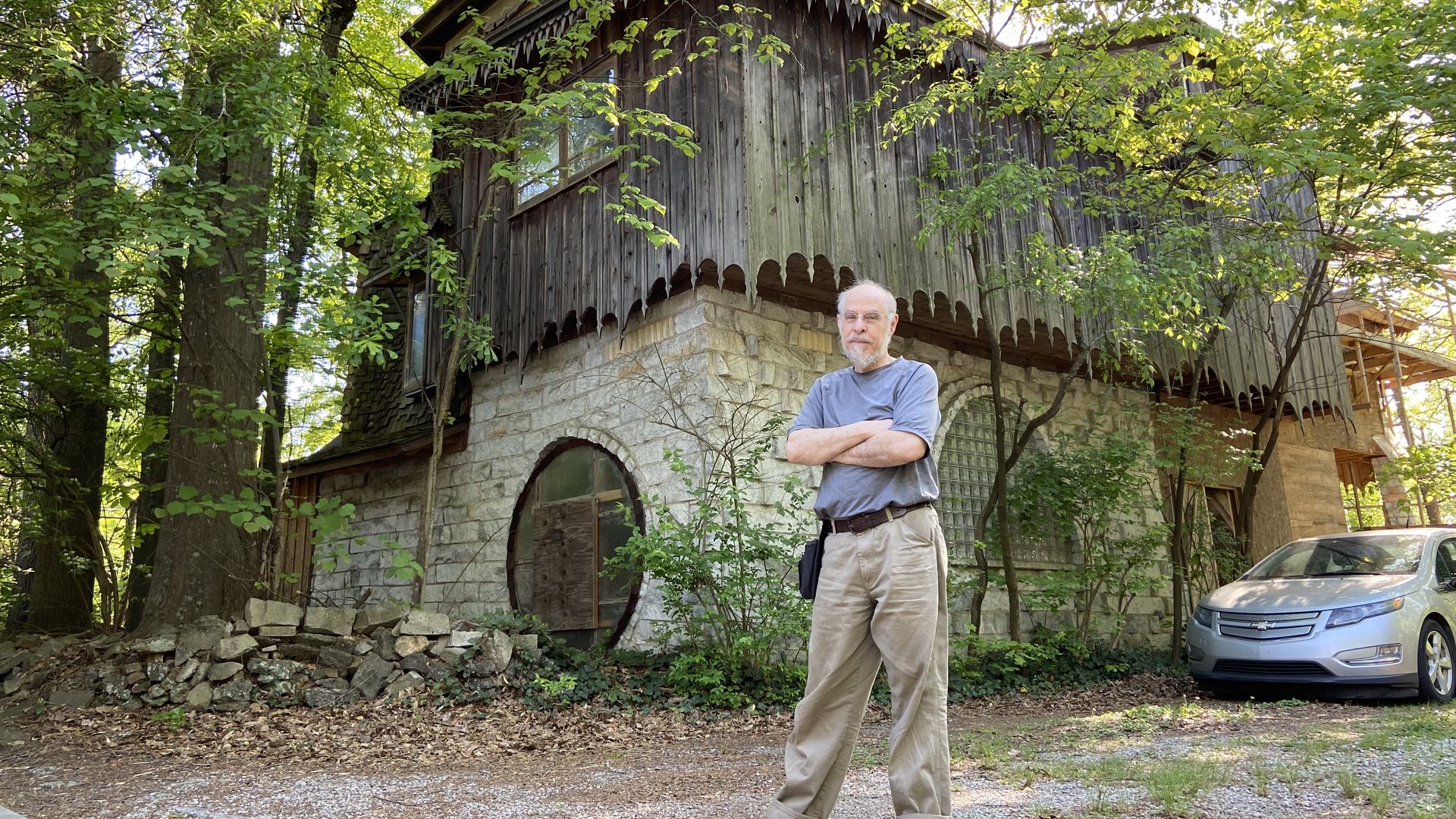 A man stands with his arms crossed in front of a large custom built home with cedar siding and marble walls