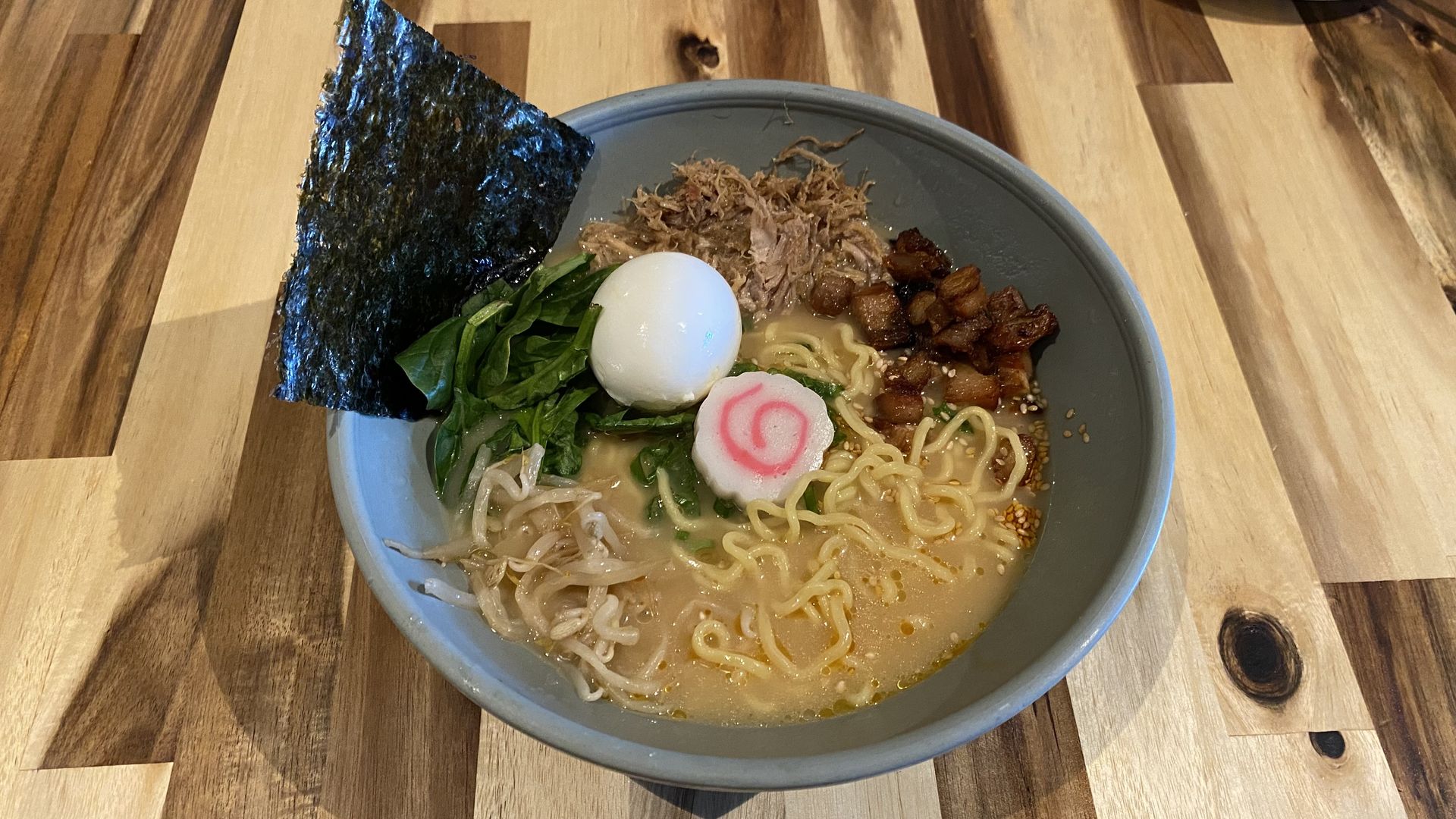 A large bowl of soup filled with noodles, meat, greens and an egg. 
