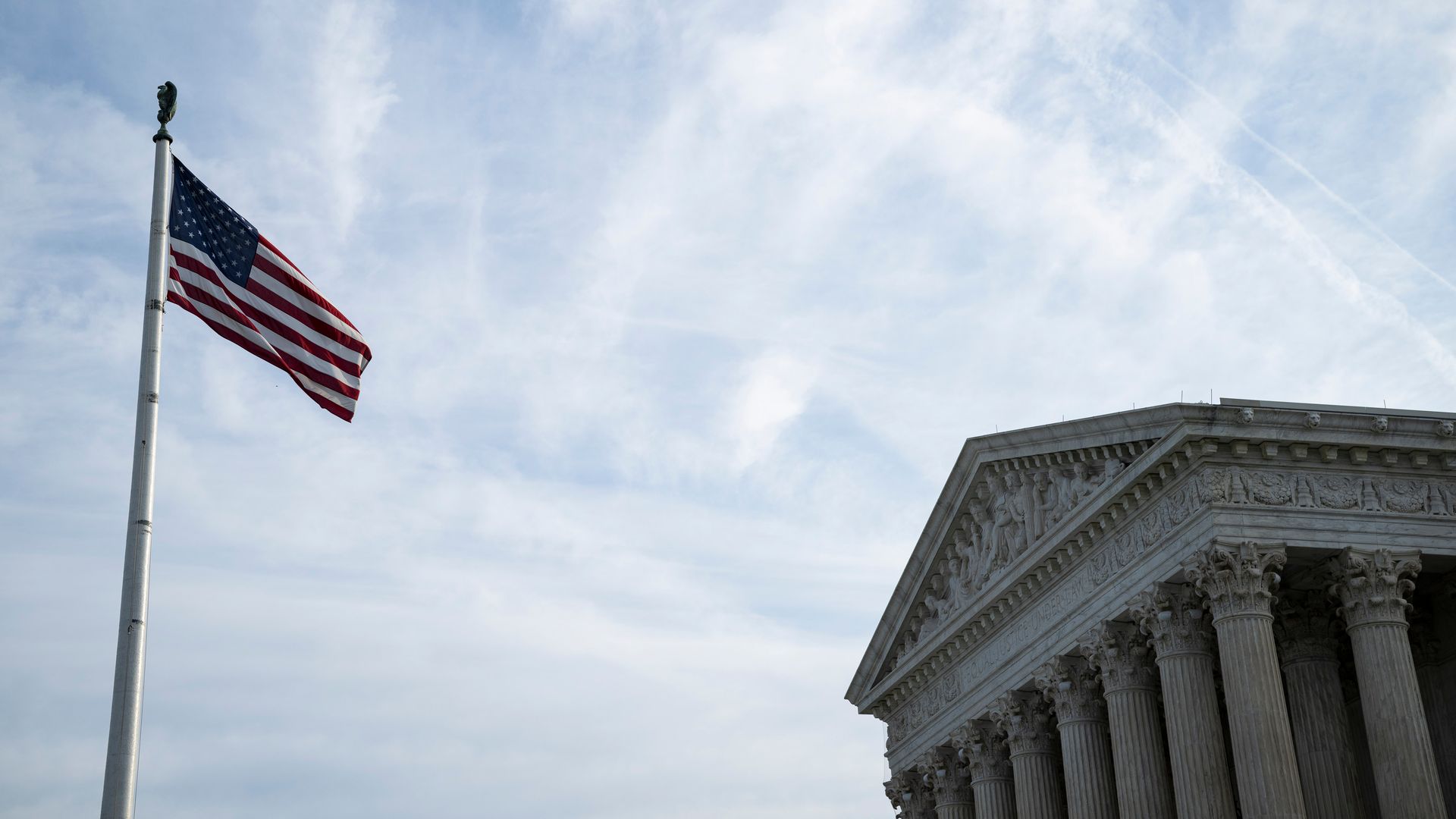 The US Supreme Court in Washington, DC, US, and an American flag waves on a flagpole.

