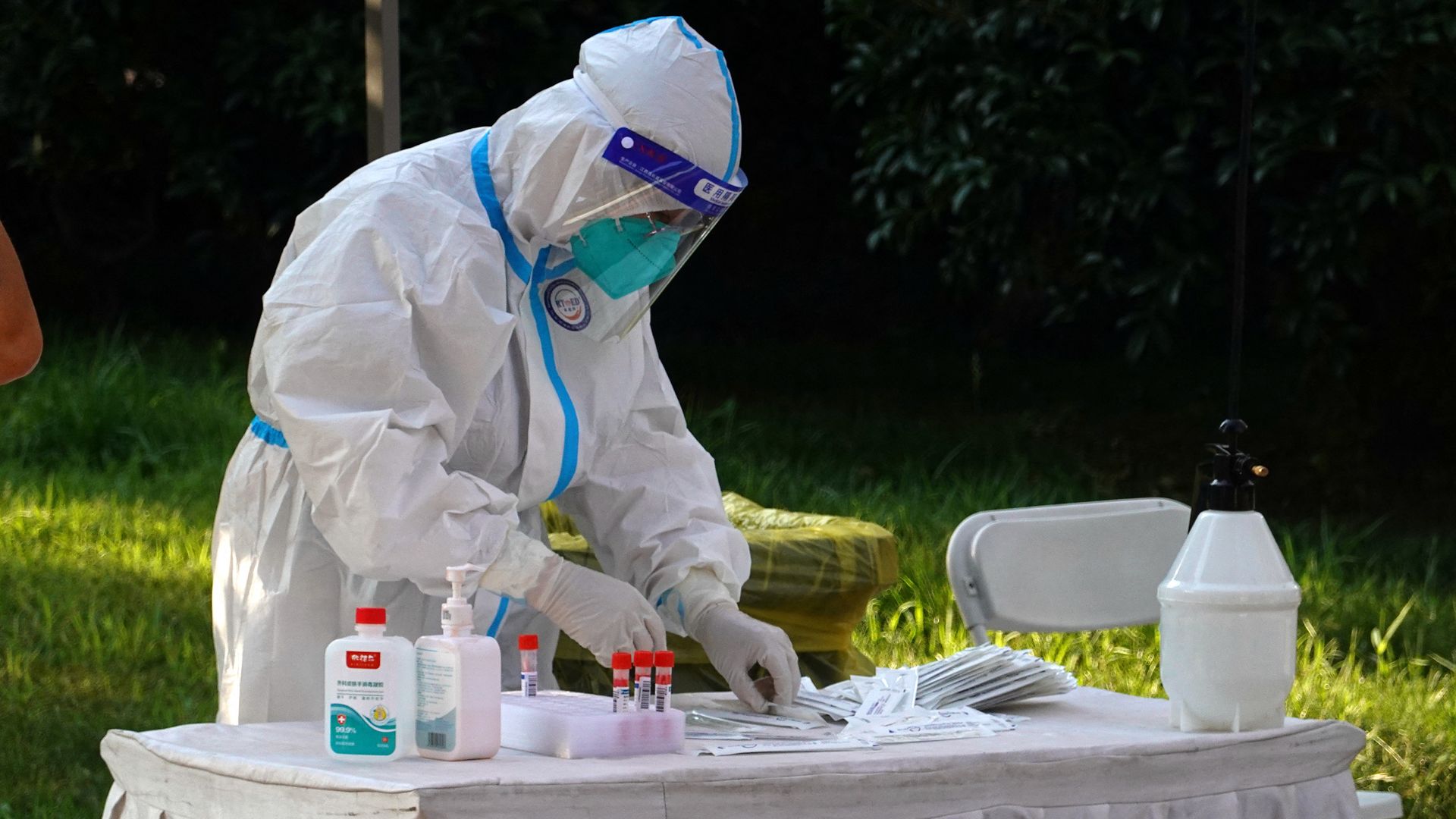 Photo of a health worker in a hazmat suit preparing testing samples on a table outside