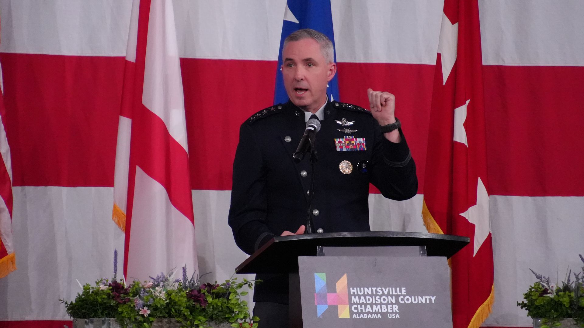 Military officer in dark uniform speaking at a podium with a 