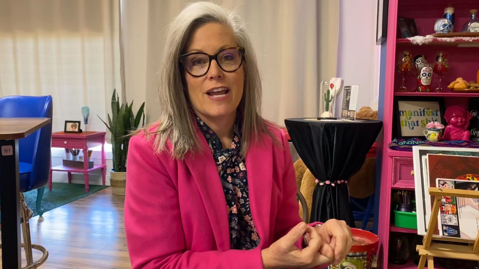 Katie Hobbs gestures with her hands while sitting and talking in a small art gallery. 