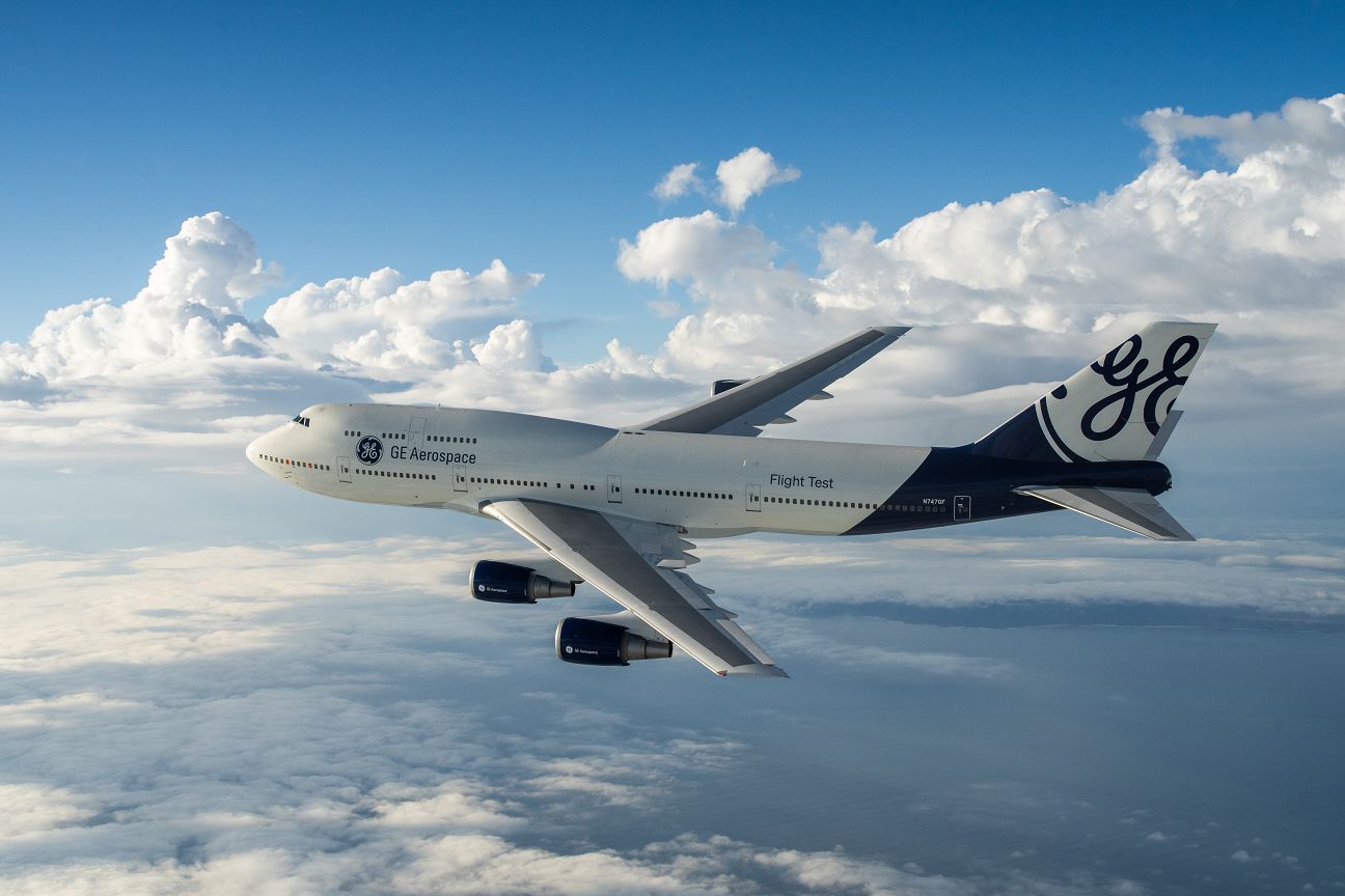 GE Aerospace wide-body aircraft in flight above clouds, four engines under the wings, white and blue livery with a large GE logo on the tail and Flight Test on the fuselage.