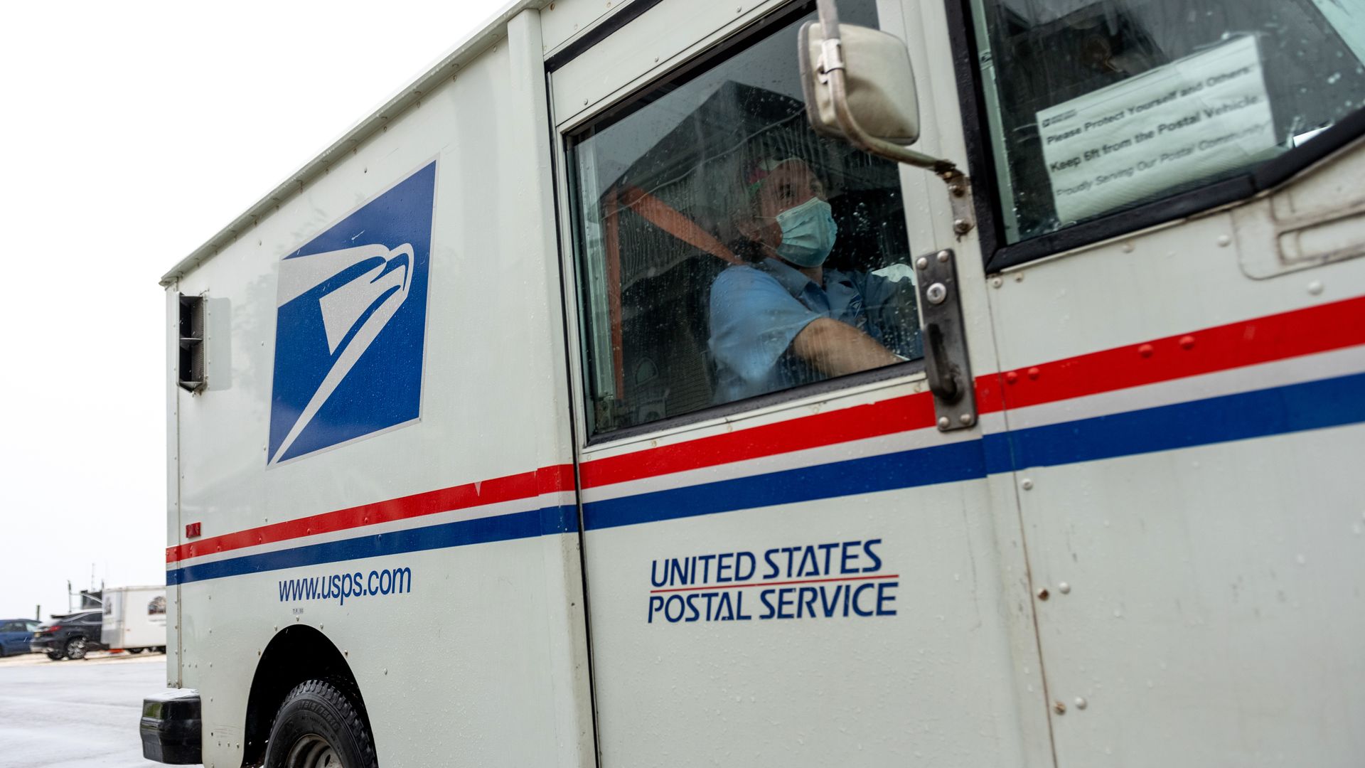 A USPS mail worker wearing a mask driving a mail vehicle on Aug. 13.