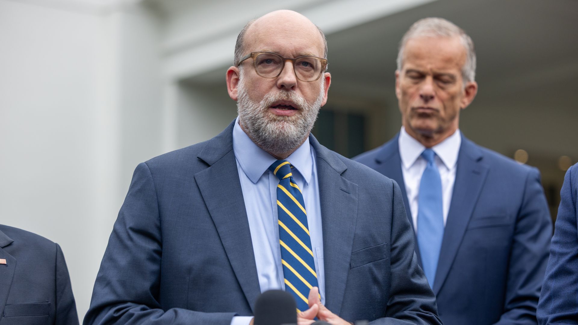 Russ Vought, a bald man with a white beard and glasses, speaks outside of the White House.