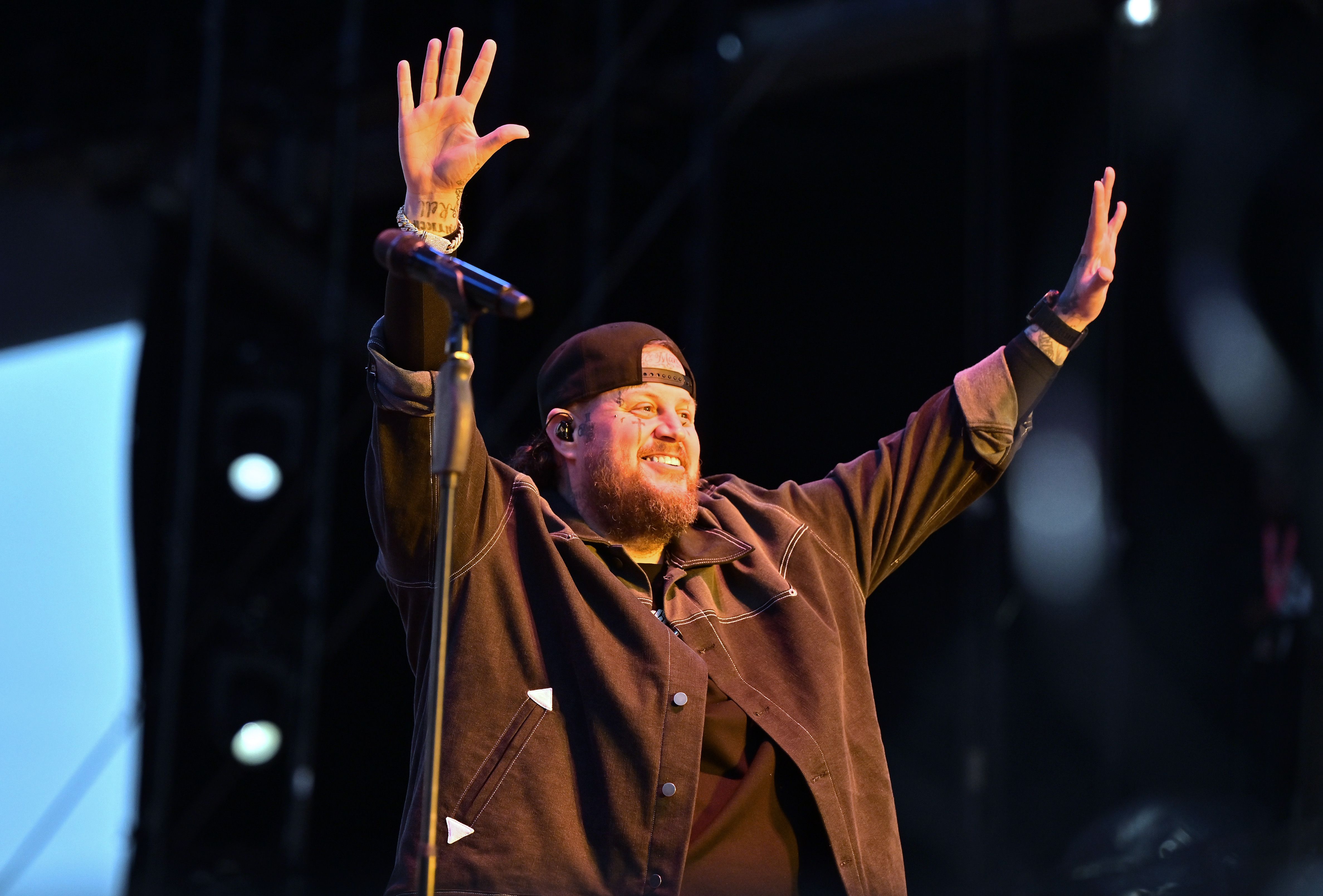 Jelly Roll performs with his hands up in the air while smiling.