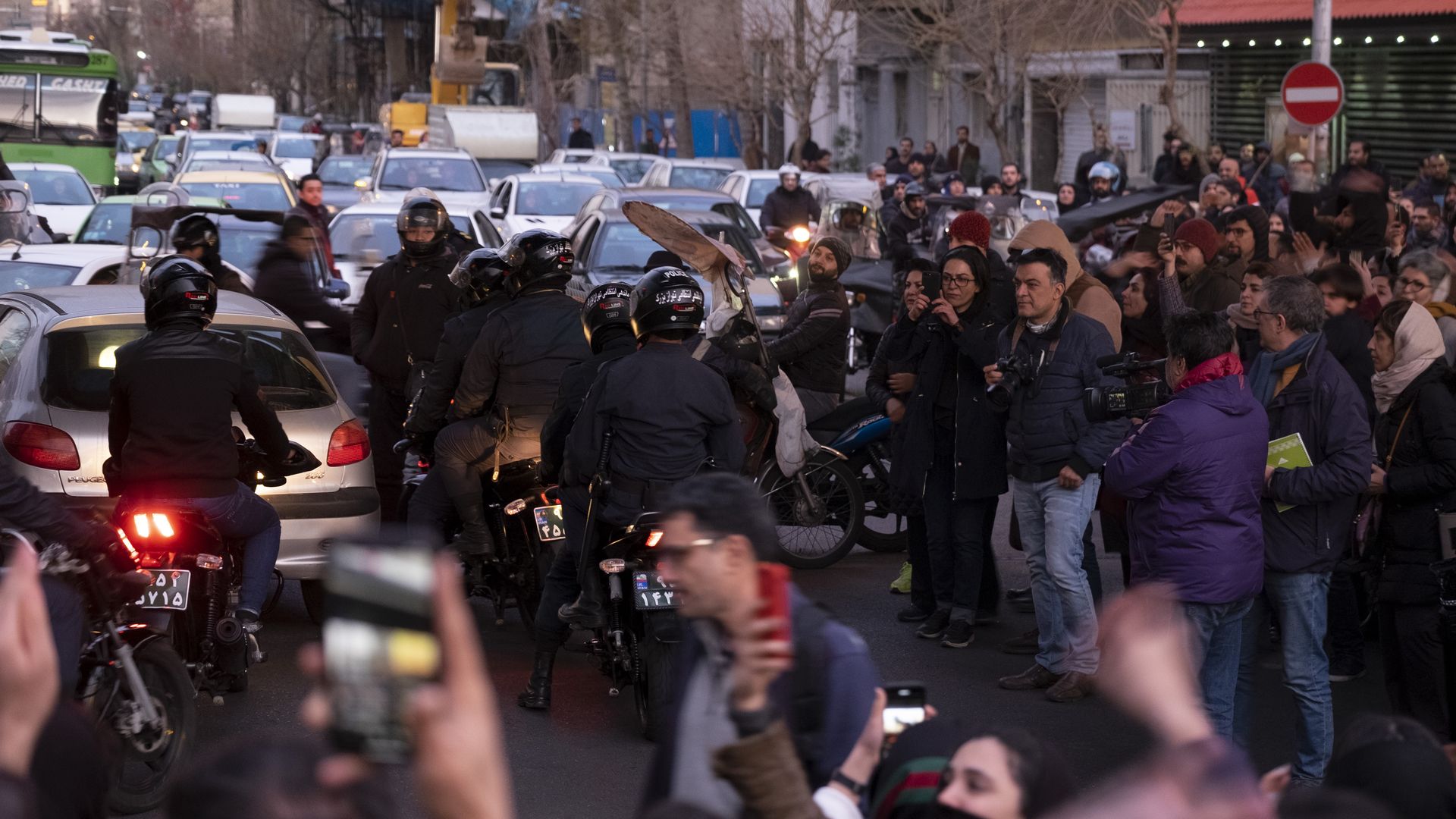 Anti-Riot policemen ride motorcycles along an avenue as Iranians gather
