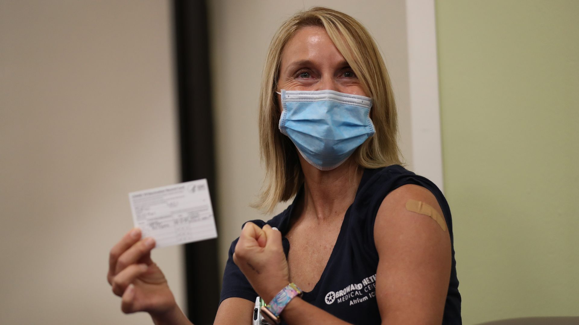 A woman holds her vaccine card after getting a shot. She is wearing a blue face mask. 
