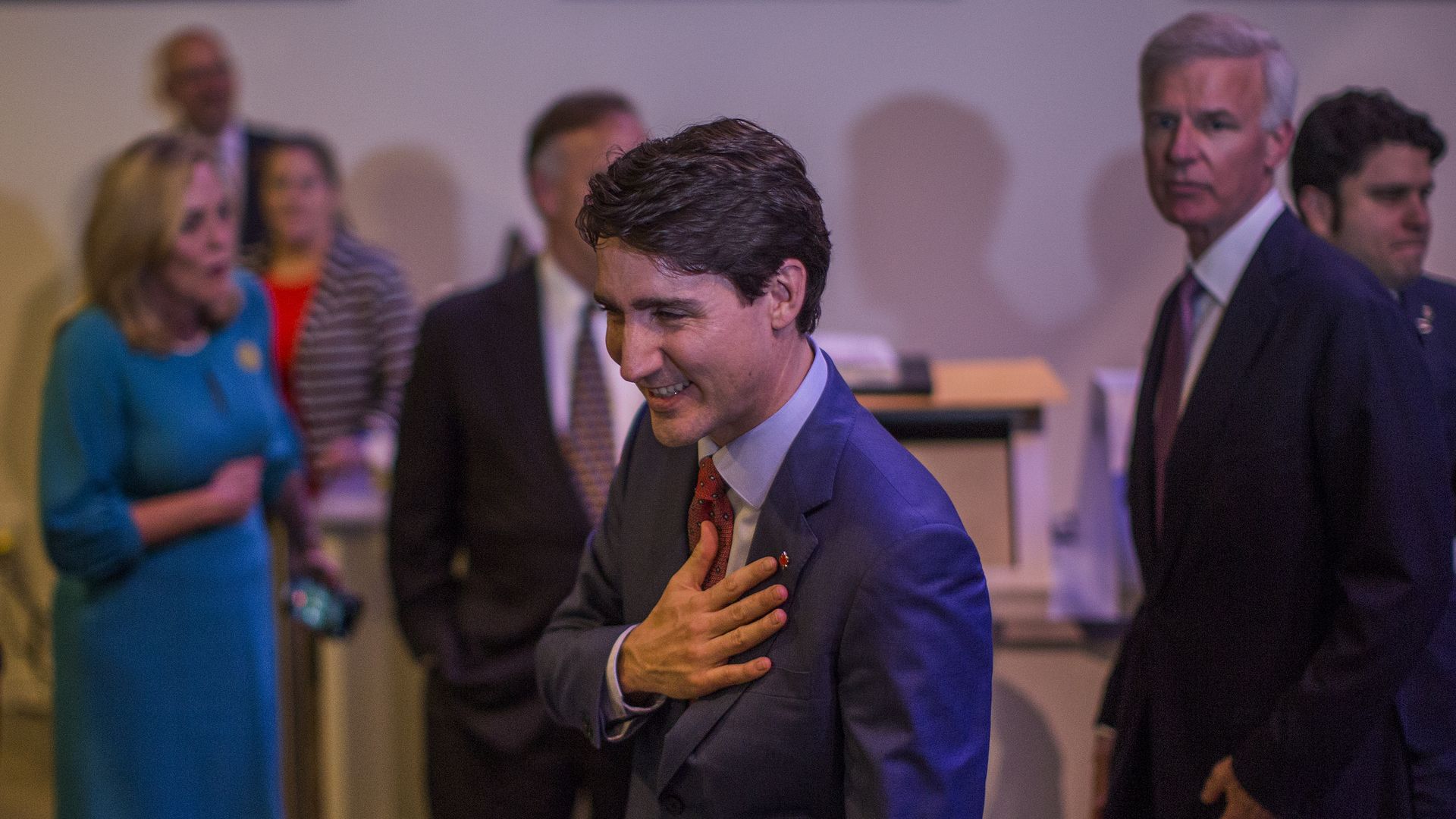 Justin Trudeau with his hand over his hear, wearing a dark grey suit with a red tie