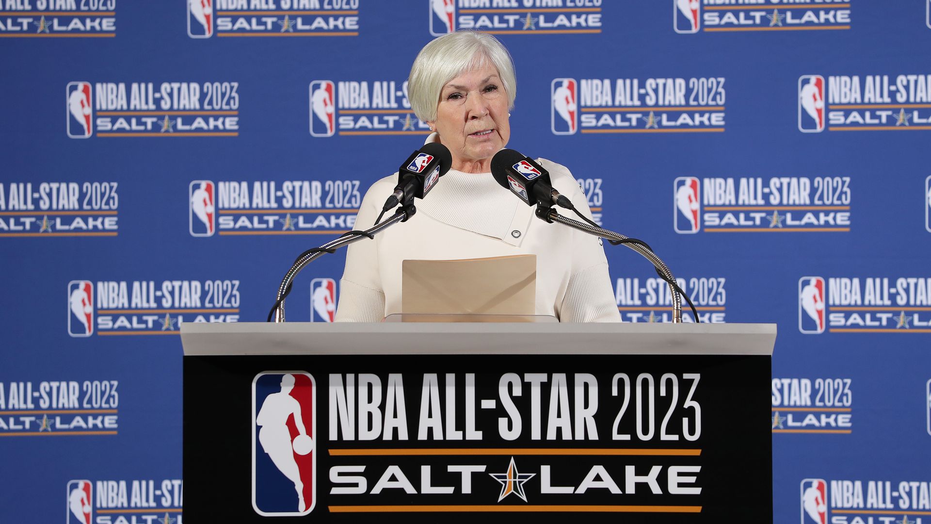 Gail Miller speaks at a podium labeled "NBA All-Star 2023 Salt Lake"